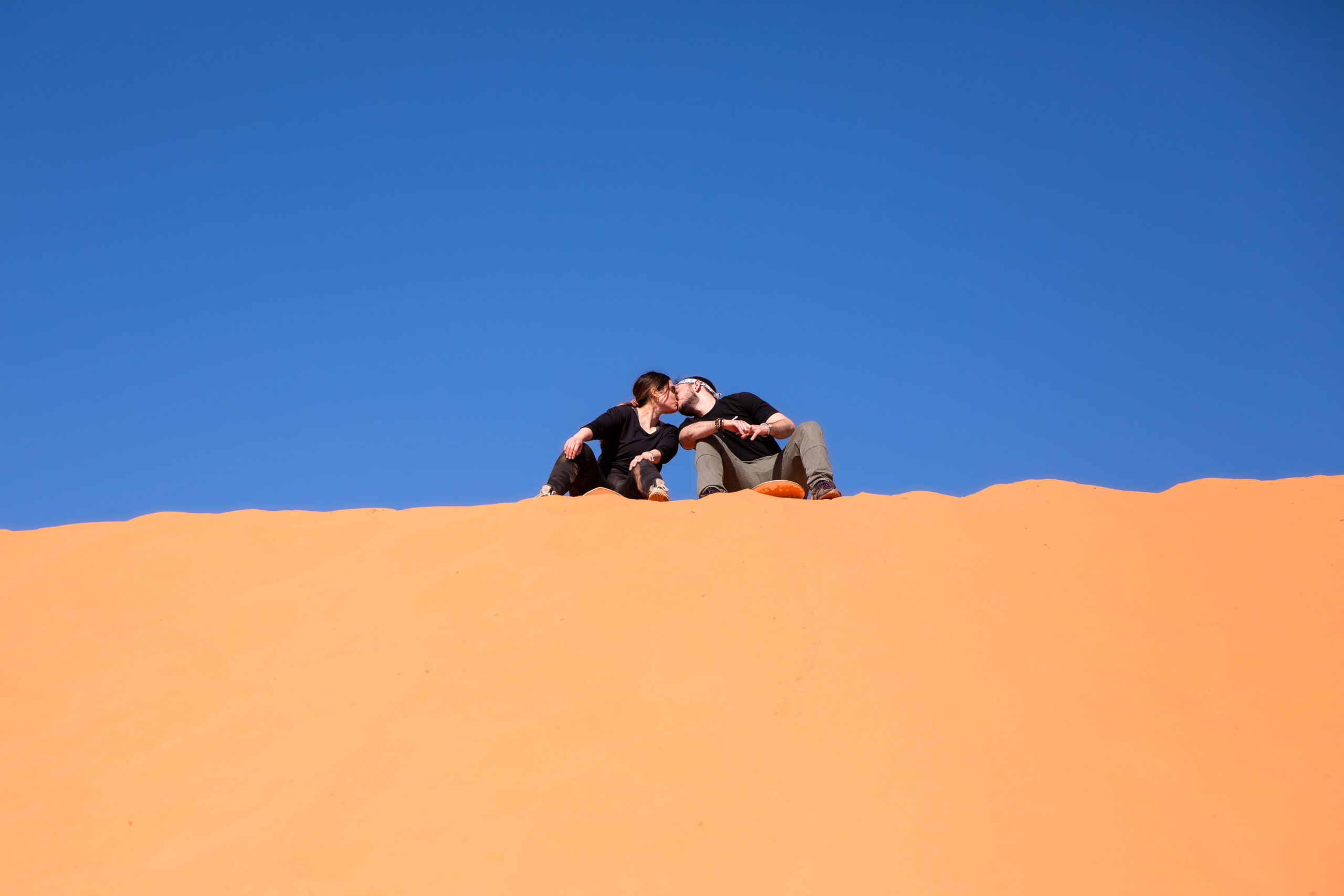 a couple kissing at the top of the sand dune after the planned proposal