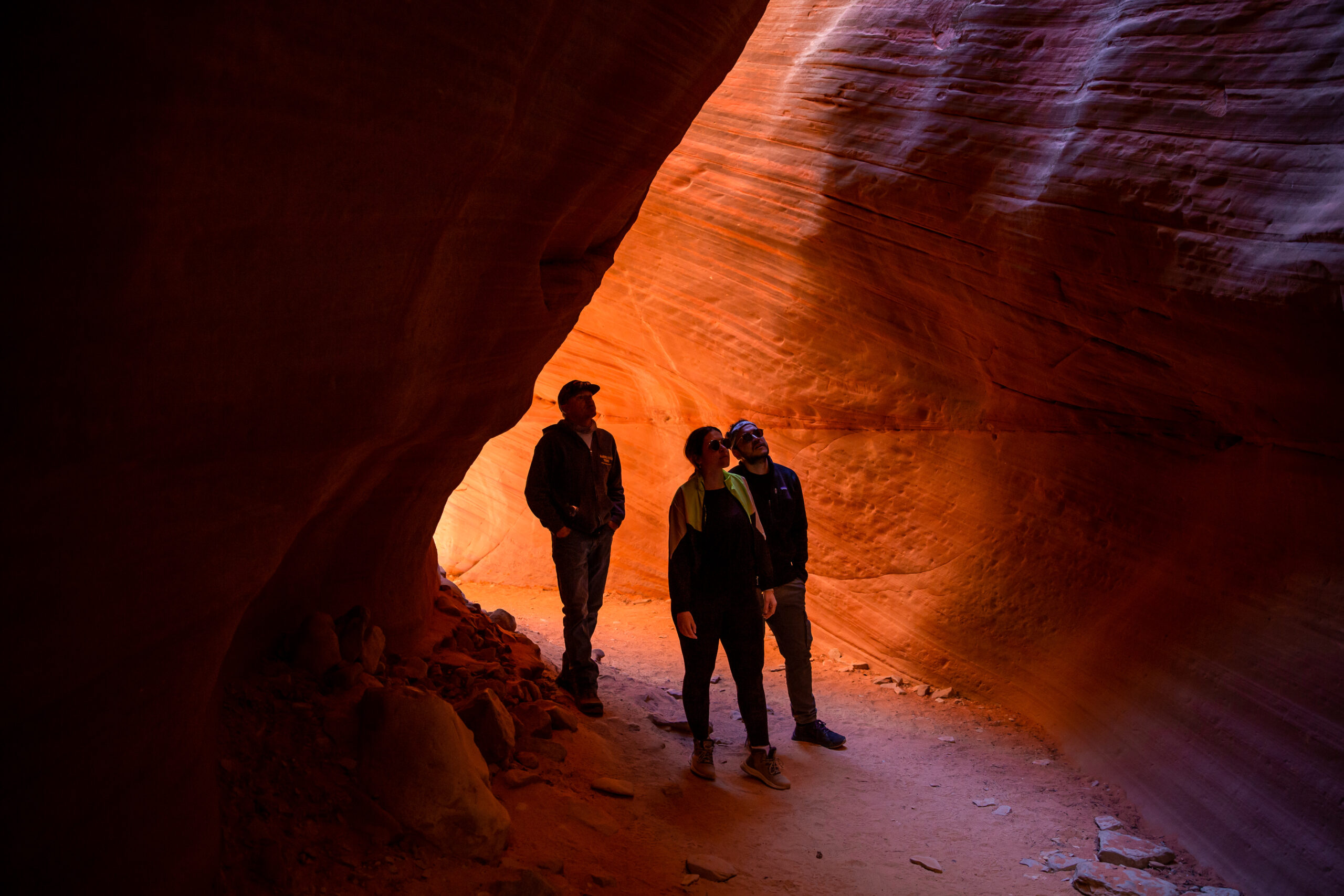 three people walking through a shaded part of the red canyon 