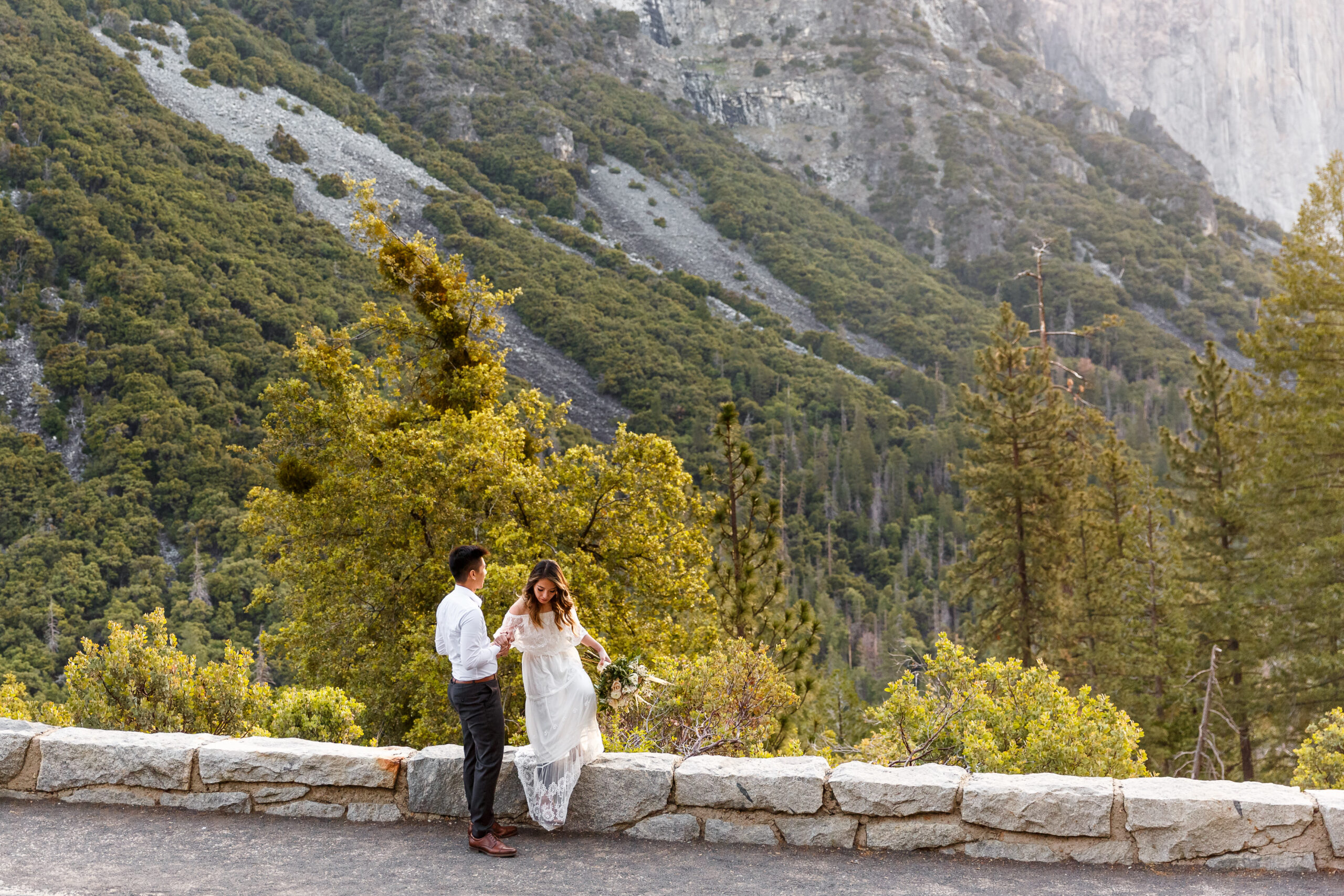 a groom helping a bride down off a ledge in Yosemite 