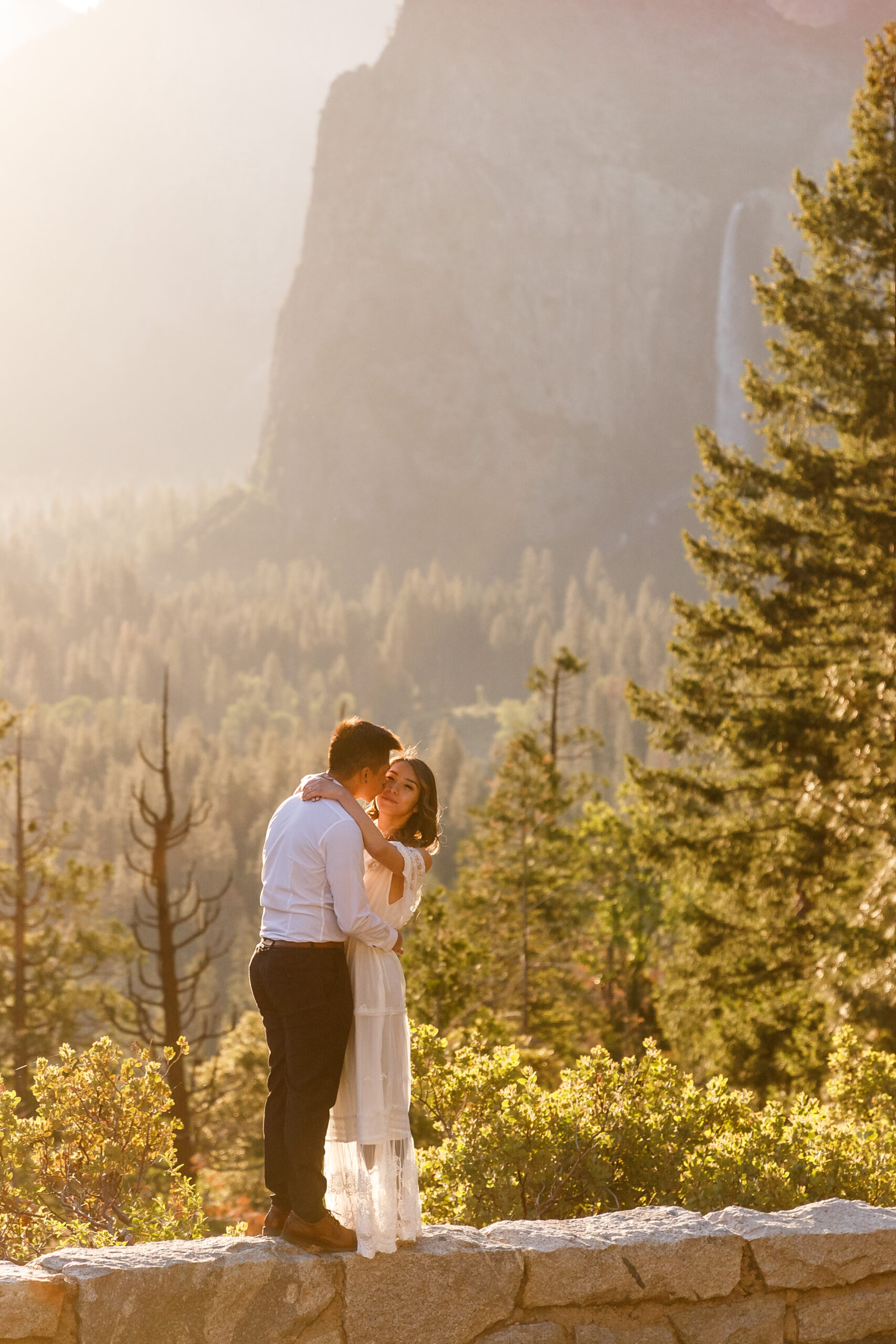 a couple standing on a ledge together during sunrise 