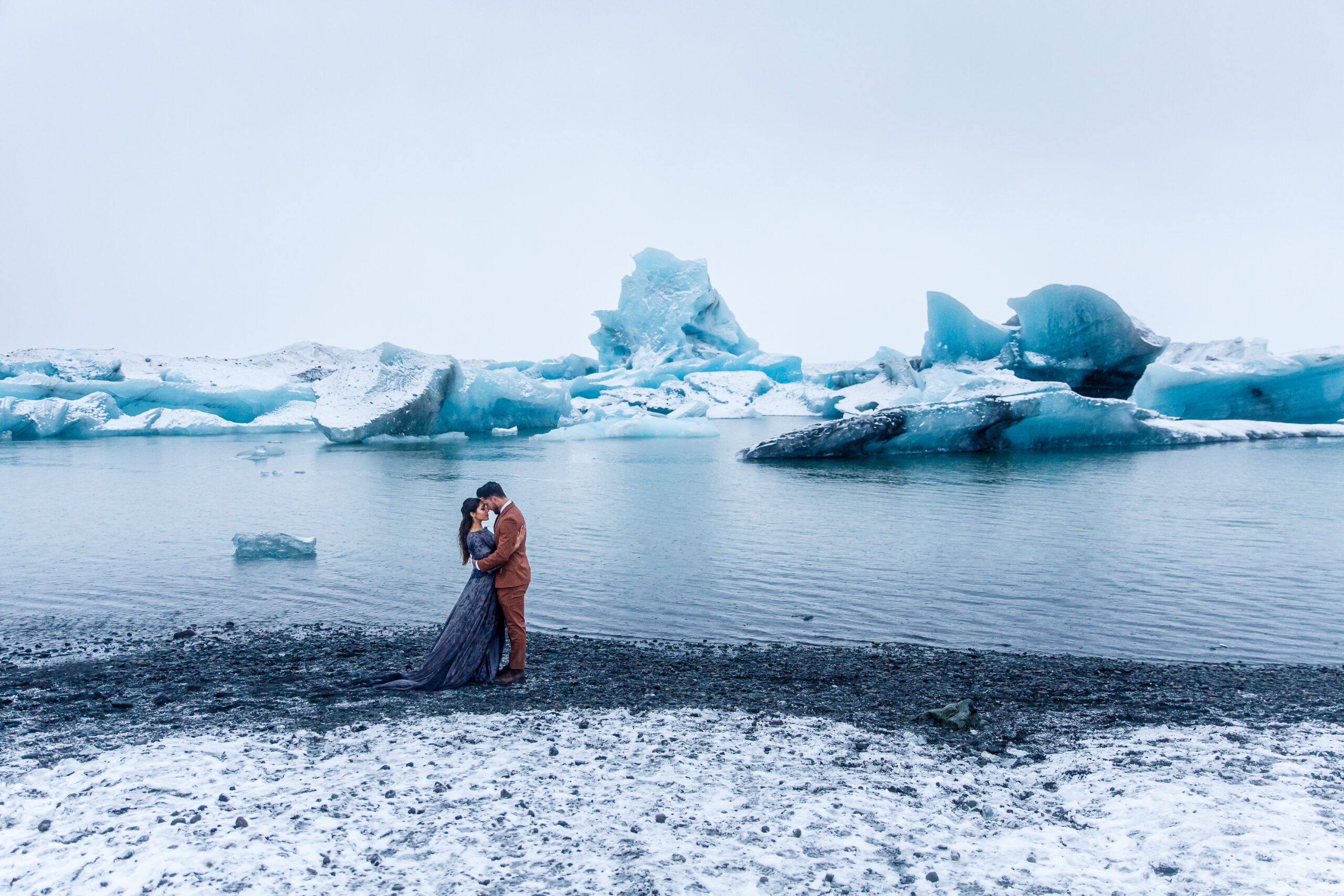 bridal couple standing on a beach with icebergs behind them 