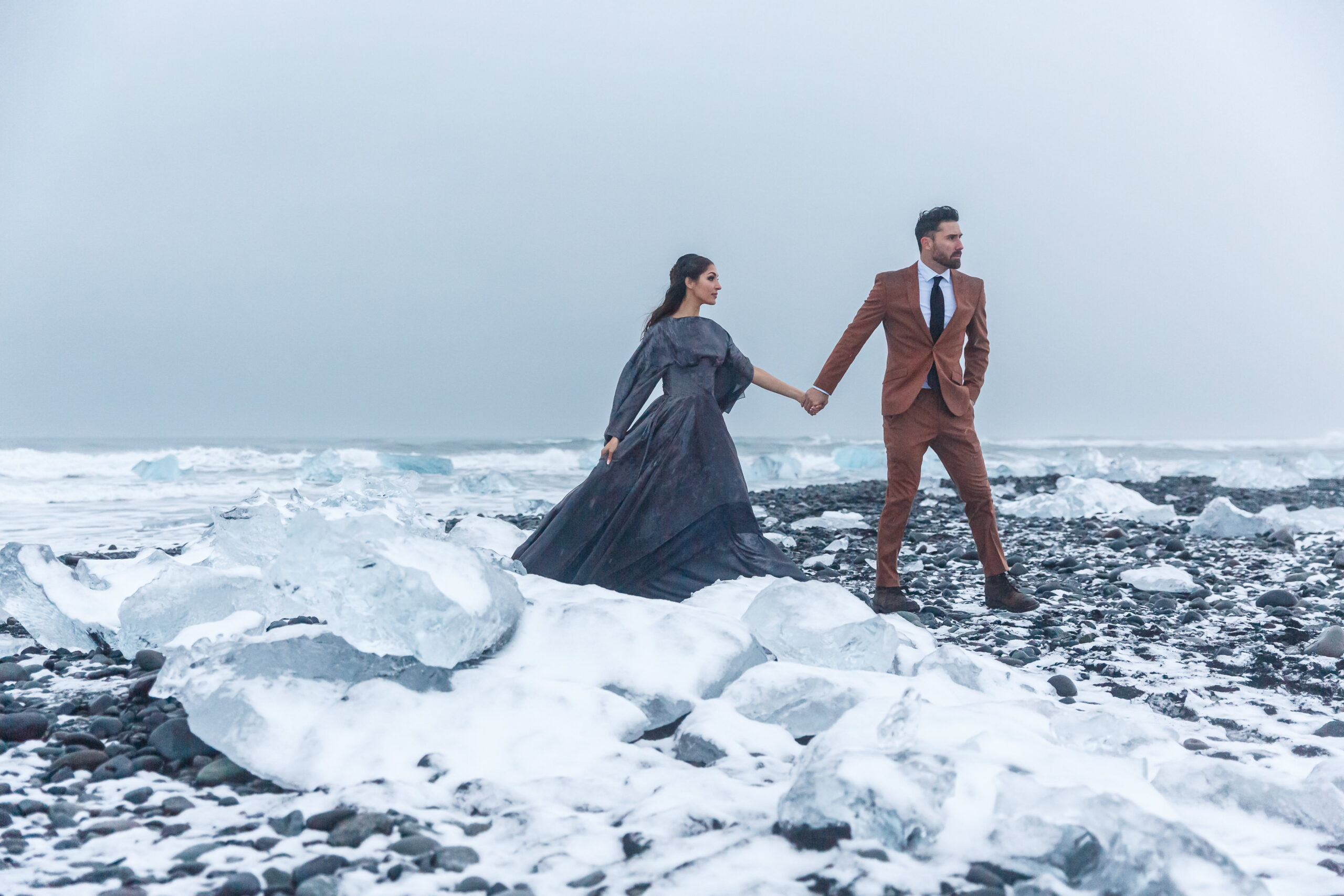 bride and groom walking hand in hand through the snow covered beach during their winter elopement