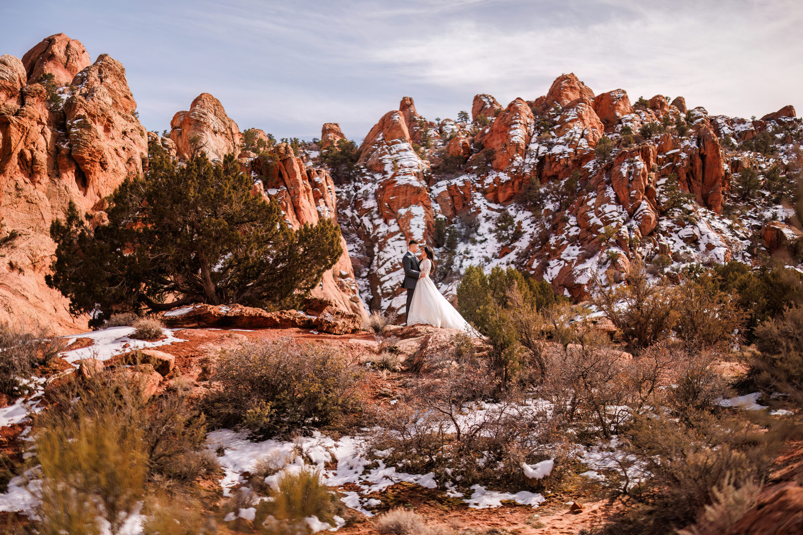 bride and groom embracing in the red rocks with snow all around them 