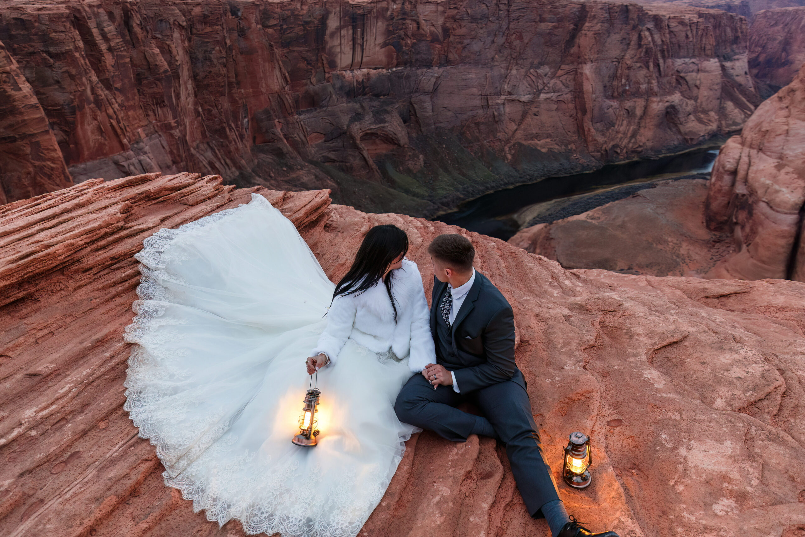 newly weds sitting on top of horseshoe bend holding lanterns and keeping warm during their winter elopement