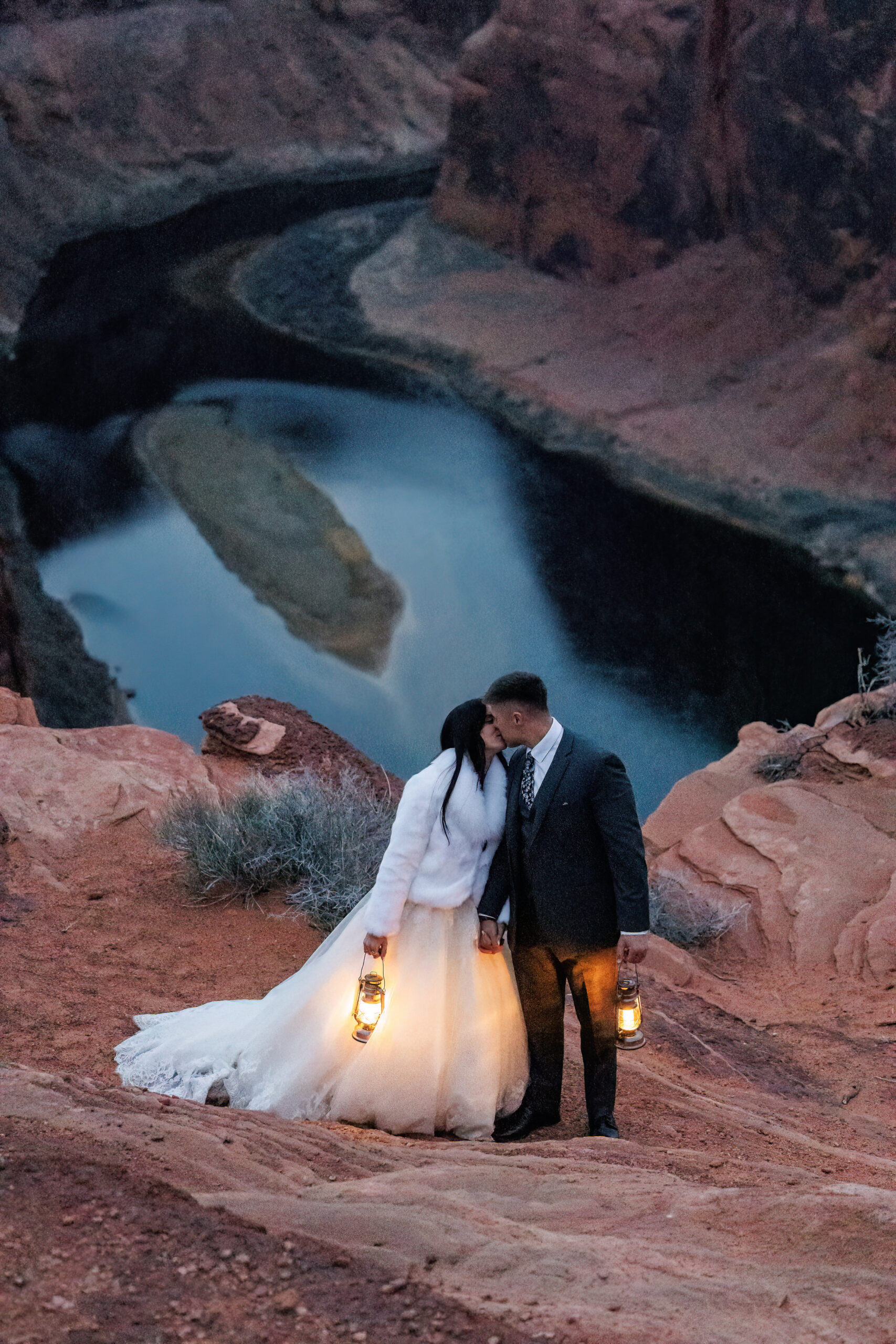 bride and groom holding lanterns and kissing on top of horseshoe bend