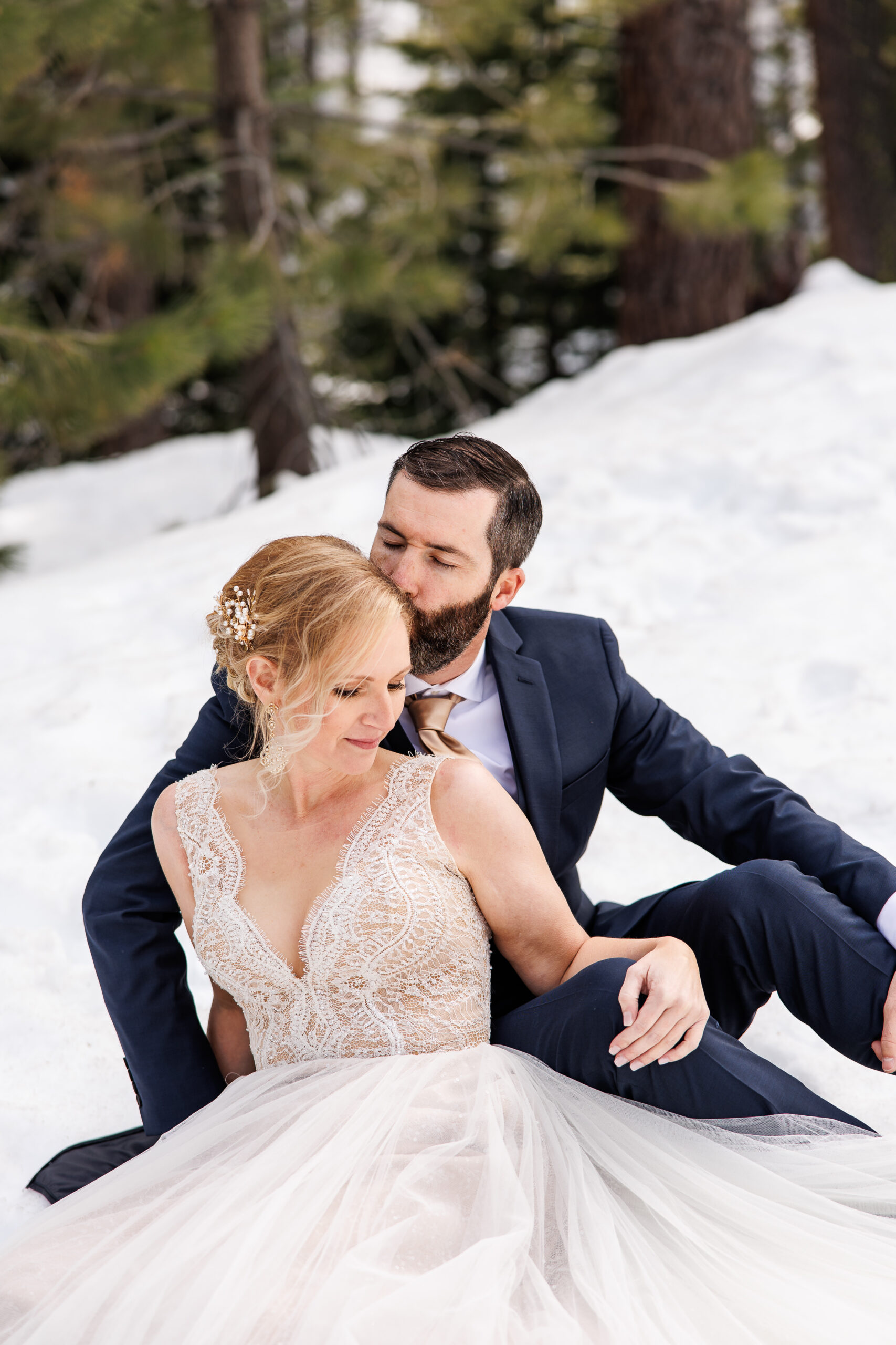 bride and groom sitting in the snow together 