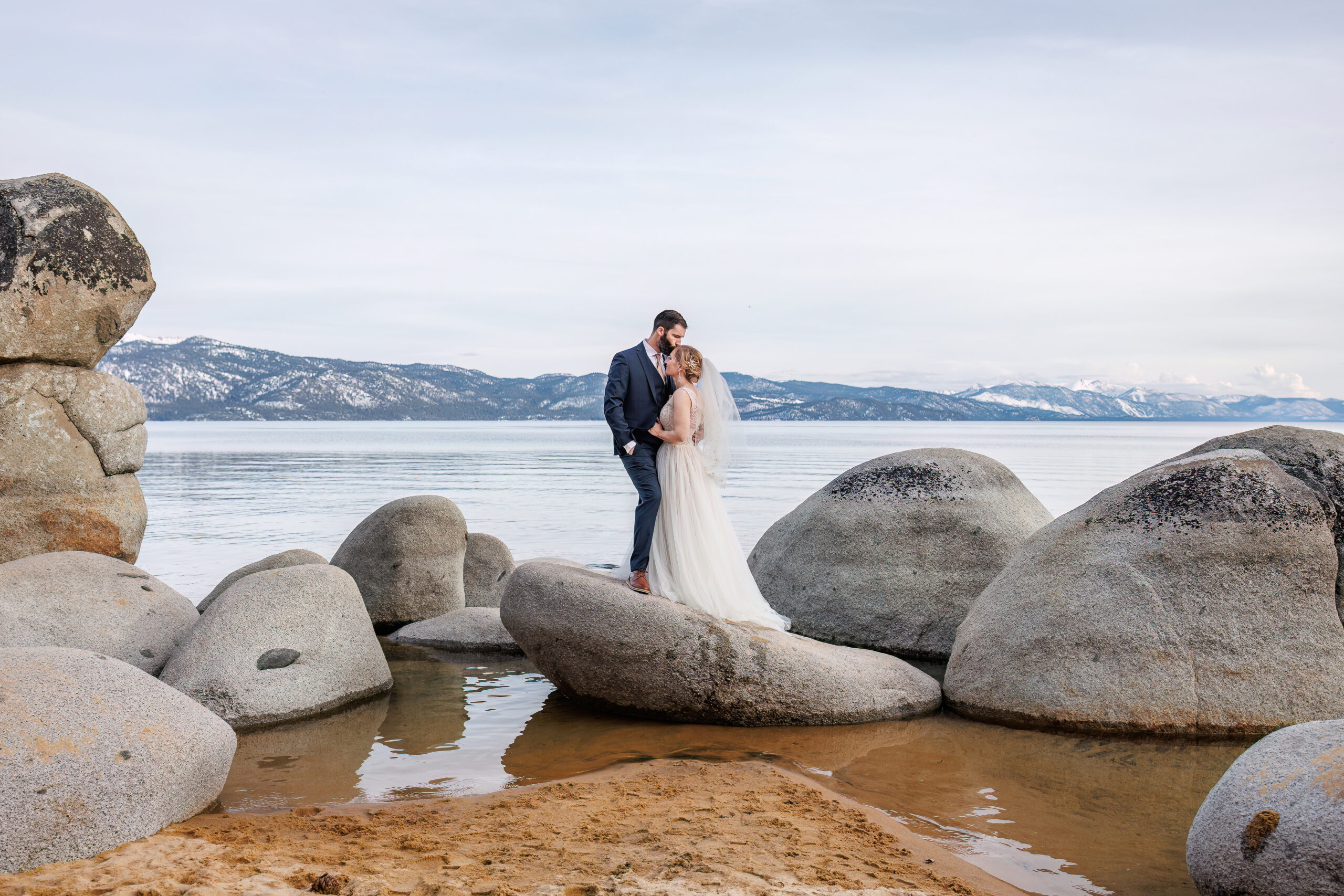 bride and groom portrait standing on big boulders by the water in lake Tahoe 