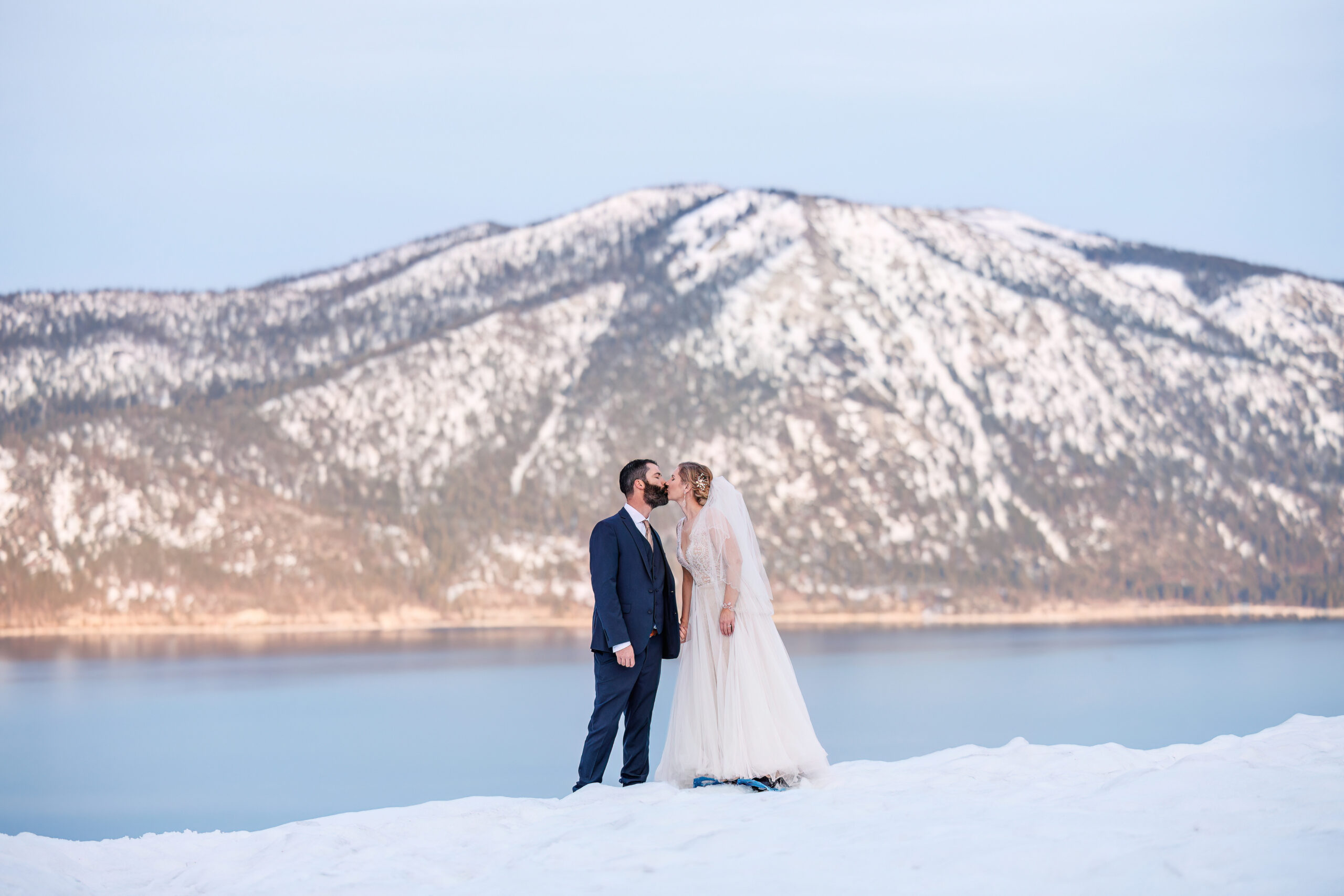 bride and groom kissing on top of the snow with mountains in the background during their winter elopement