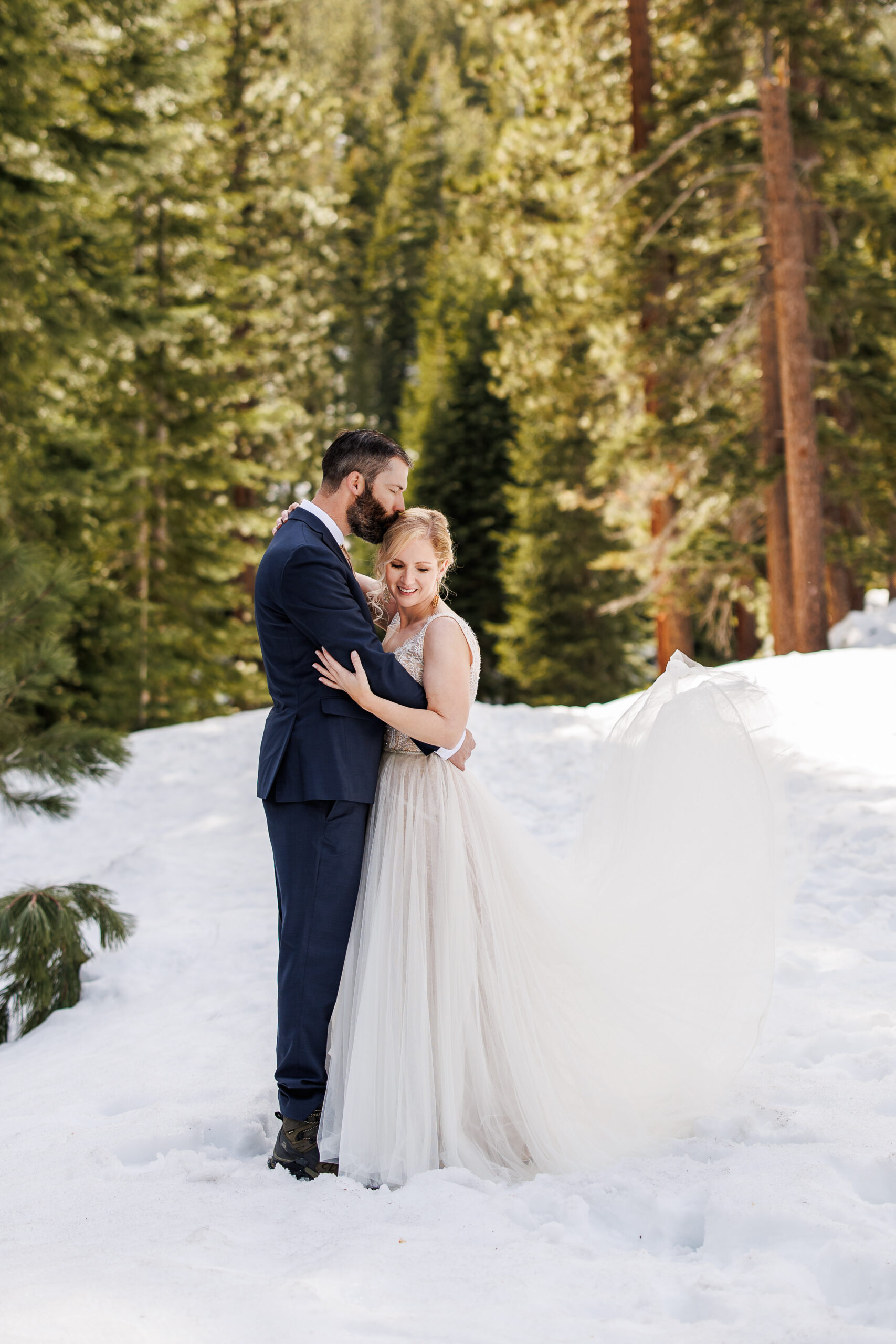 groom kissing bride on the head as they stand in the snow for their winter elopement