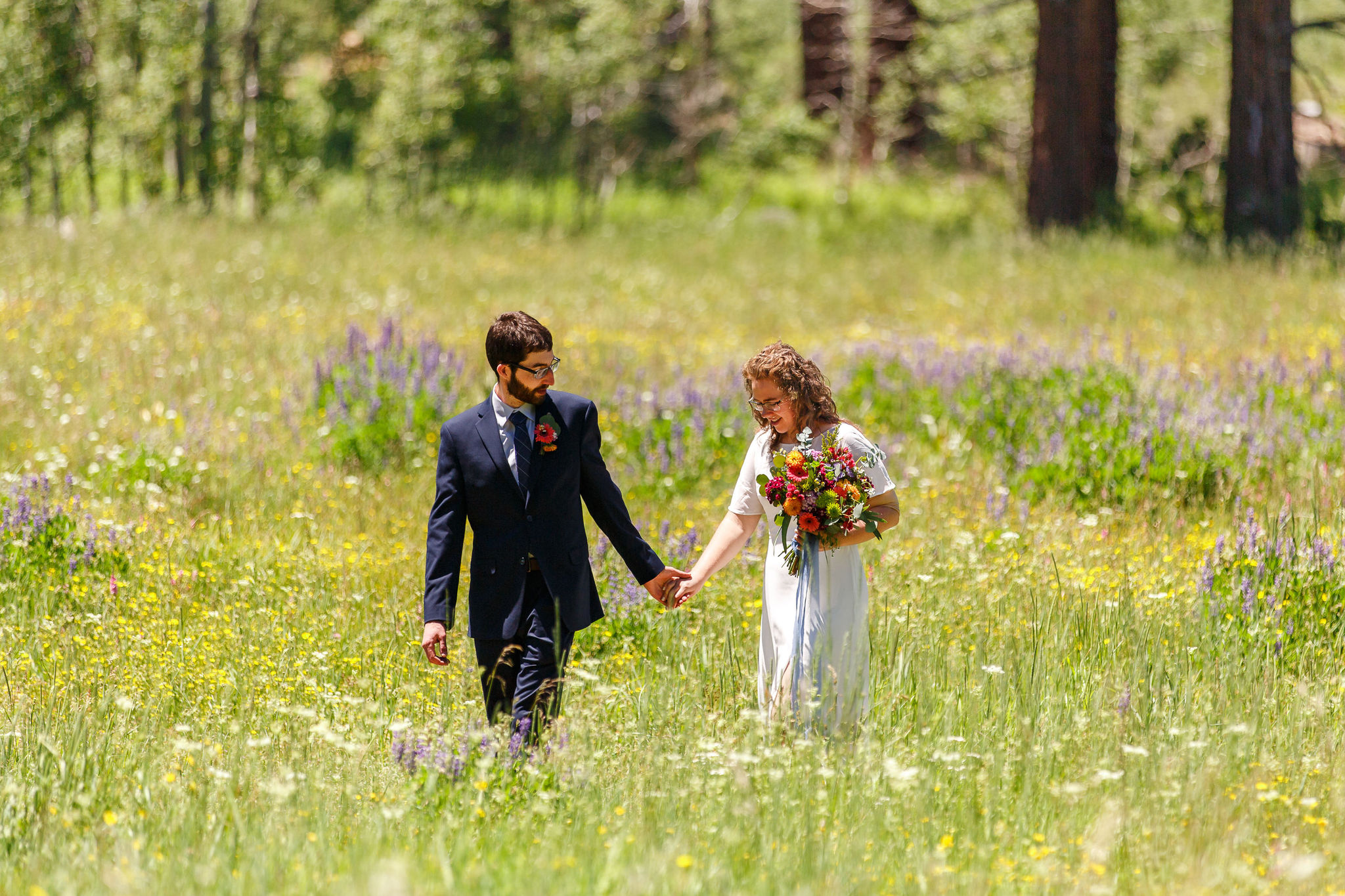 bride and groom walking hand in hand through the meadow after their ceremony 