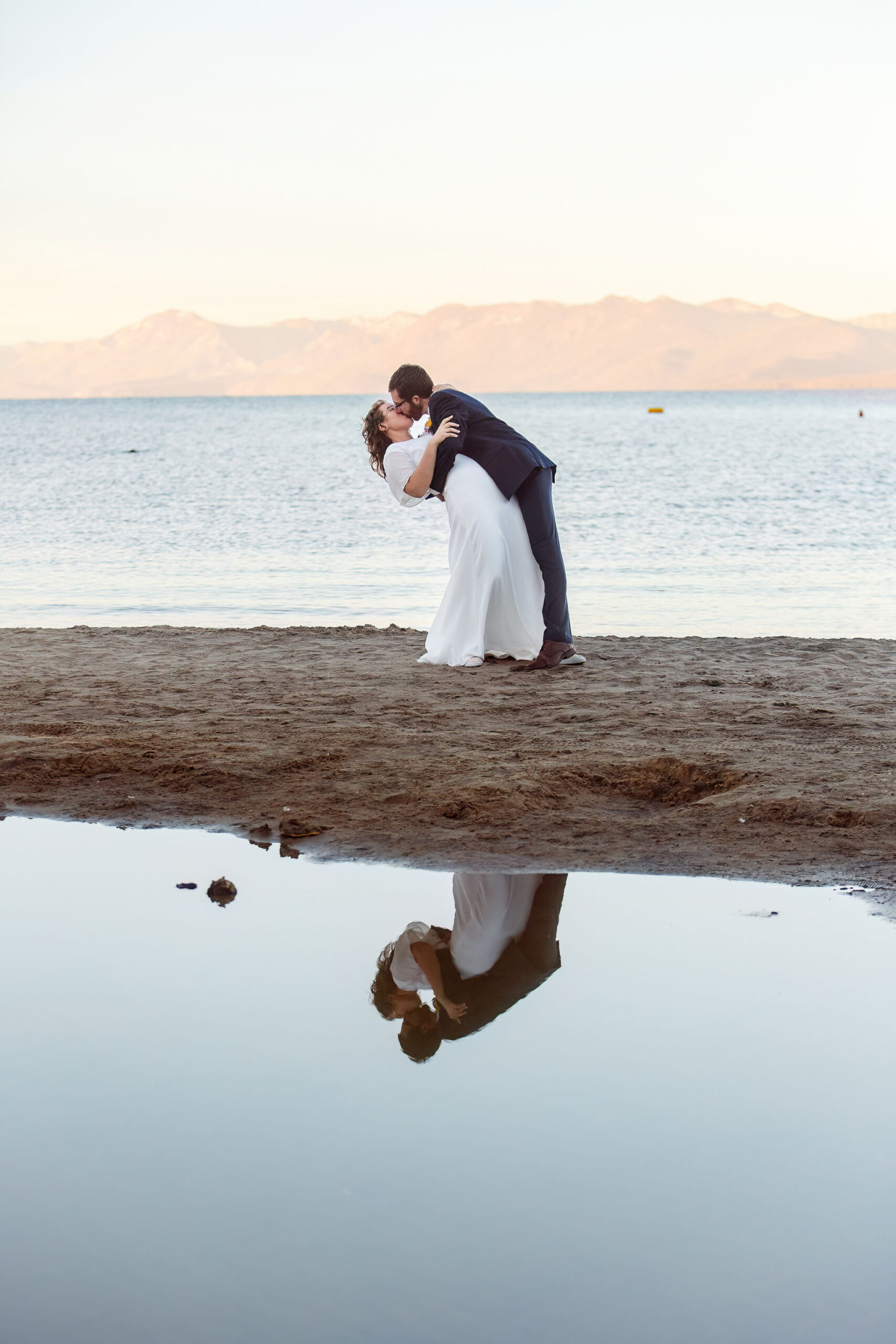 groom dipping and kissing his bride with their reflection in Lake Tahoe