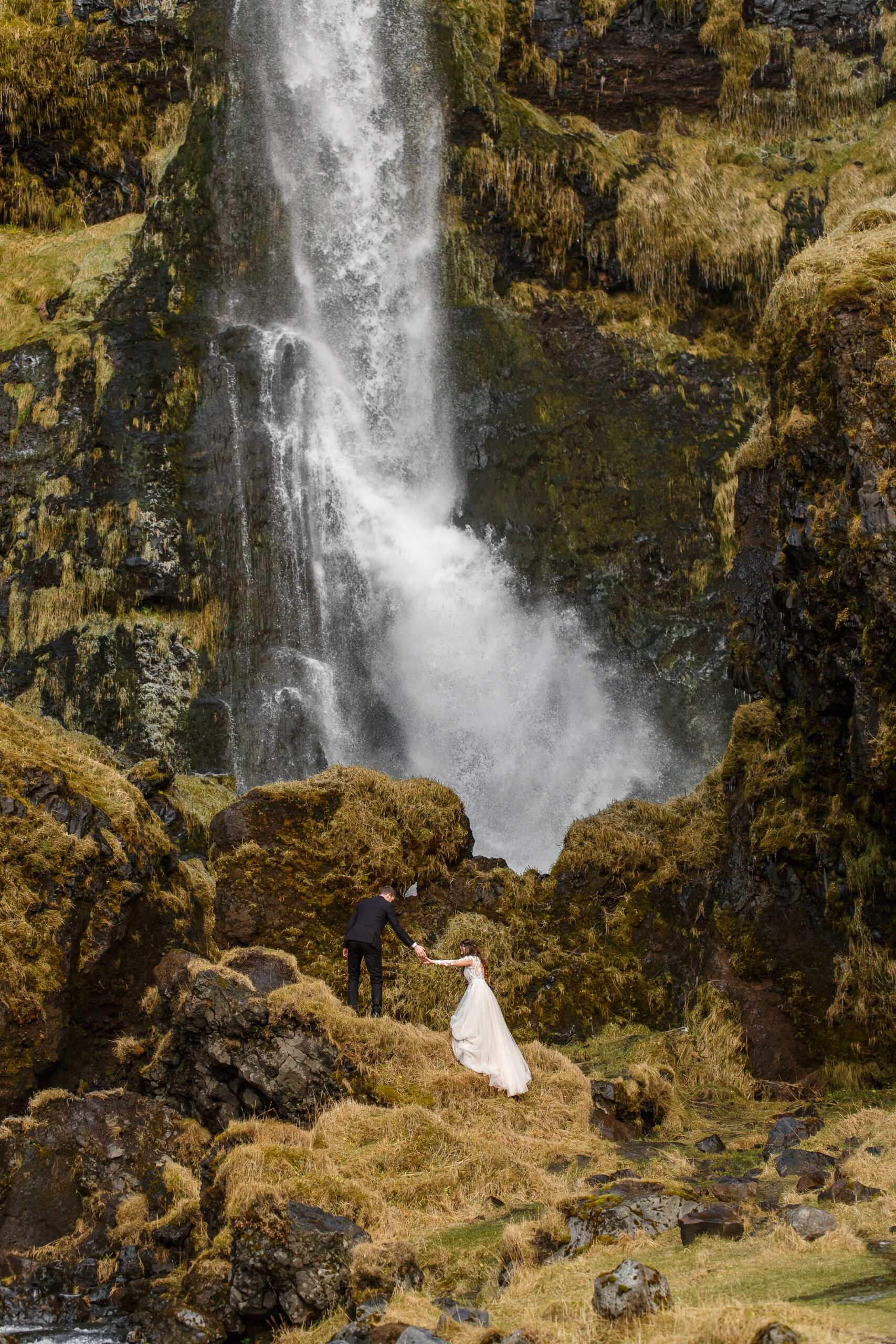 bride and groom walking up to the waterfall in Iceland 