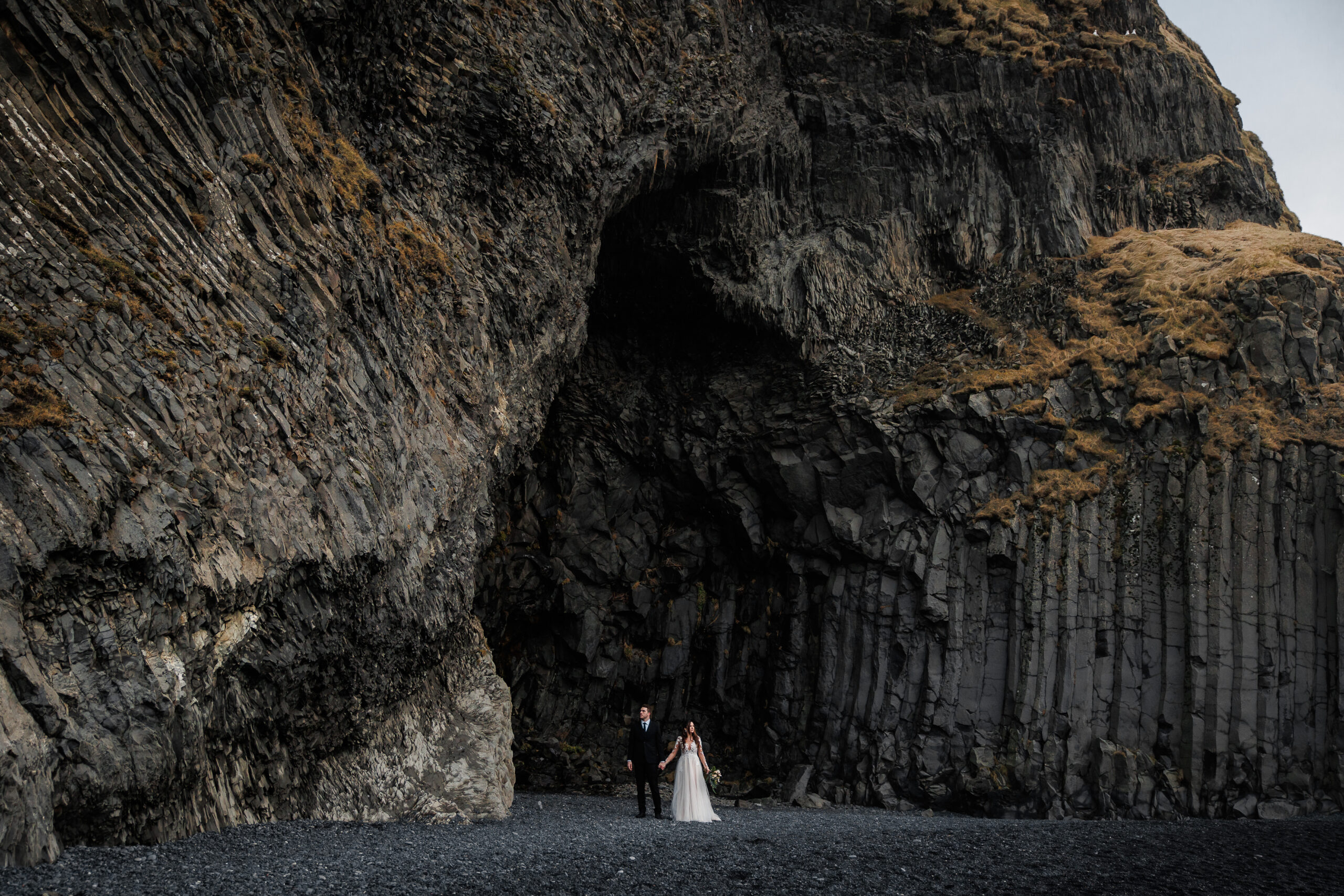 newly weds standing hand and hand on a black beach for their winter elopement