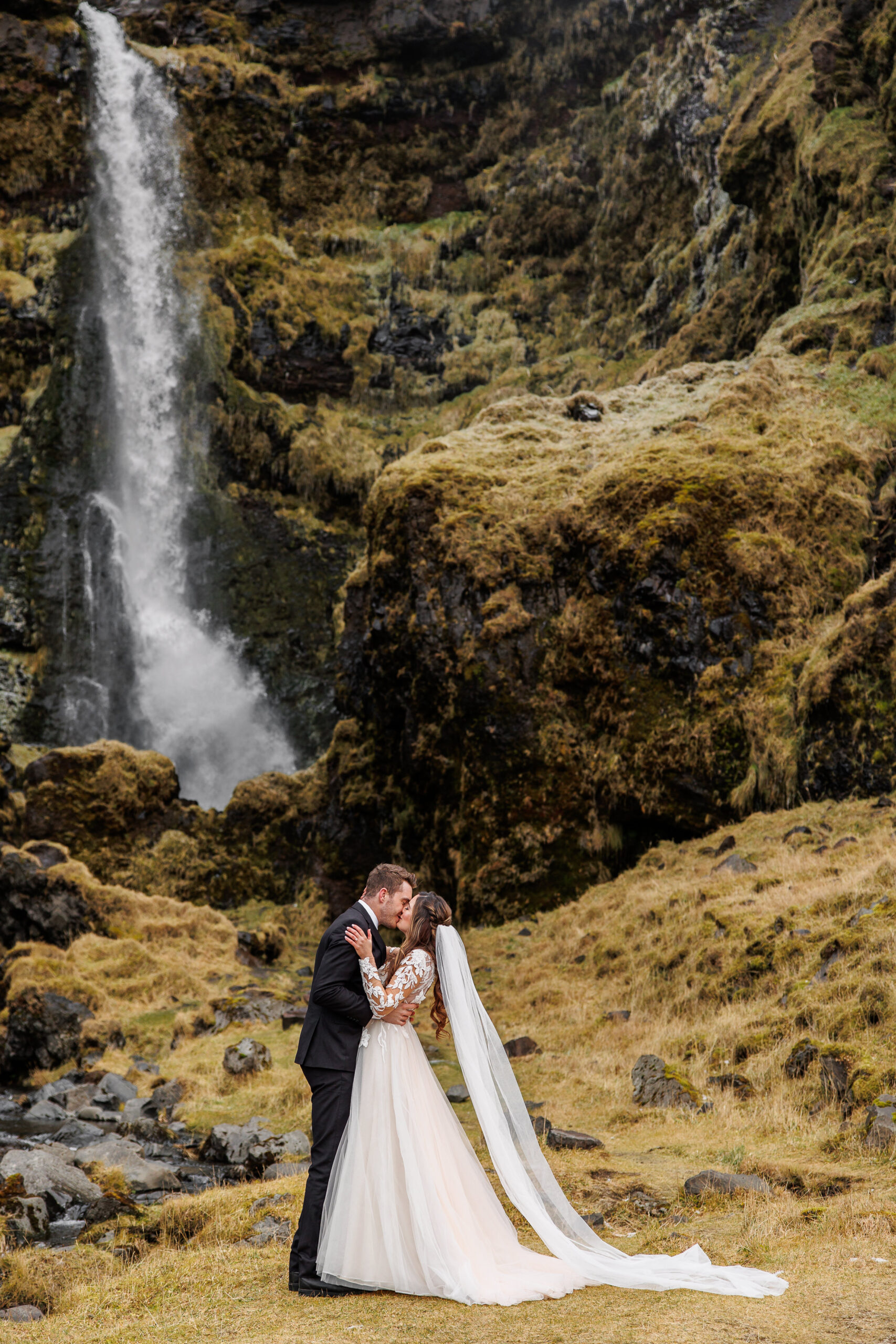 bride and groom kissing in front of the waterfall after the winter elopement ceremony 