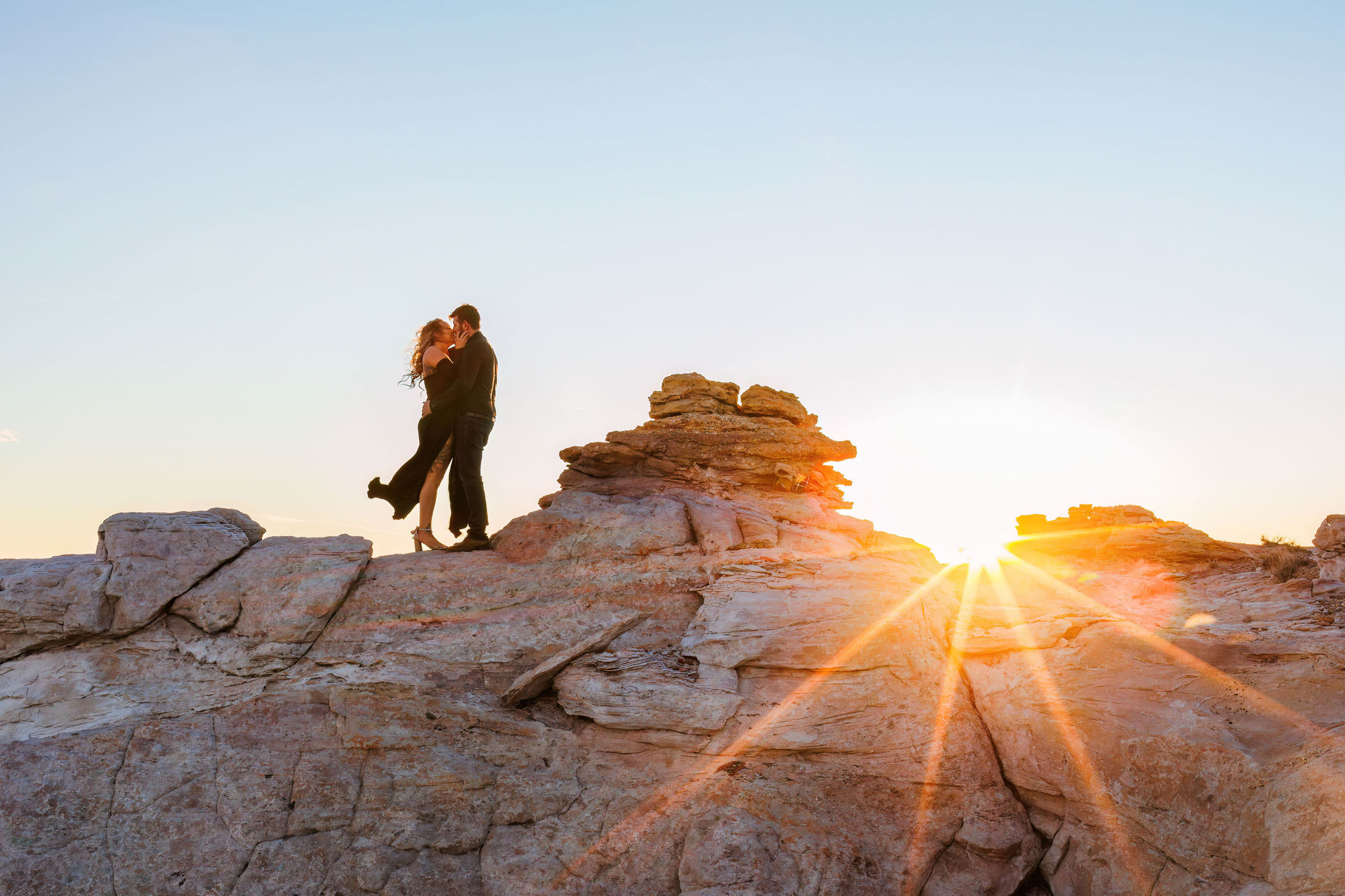 a couple kissing on the rocks as the wind whips through their hair 