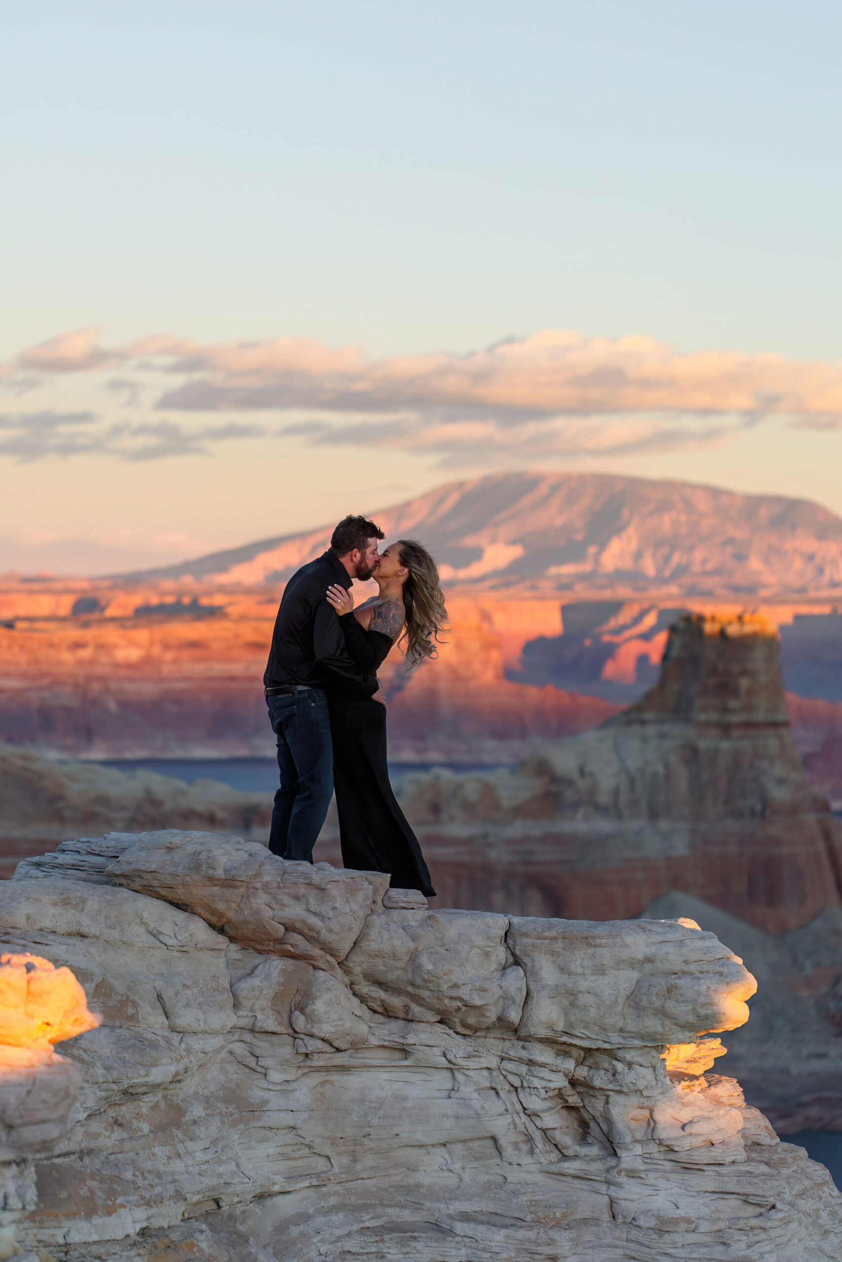 a newly engaged couple kissing as the sun dips down creating cotton candy skies 