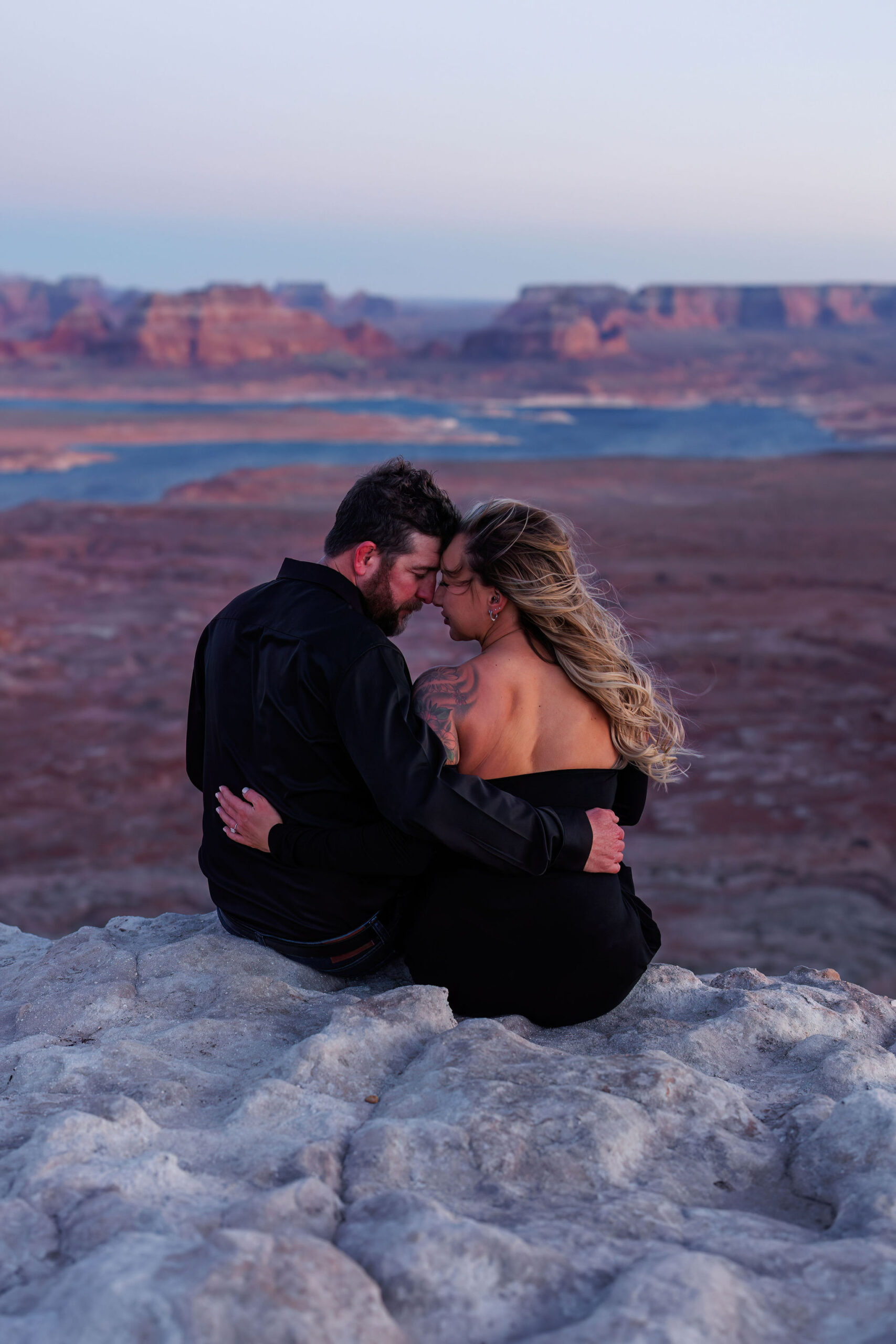 newly engaged couple sitting on a rock ledge with their foreheads together 