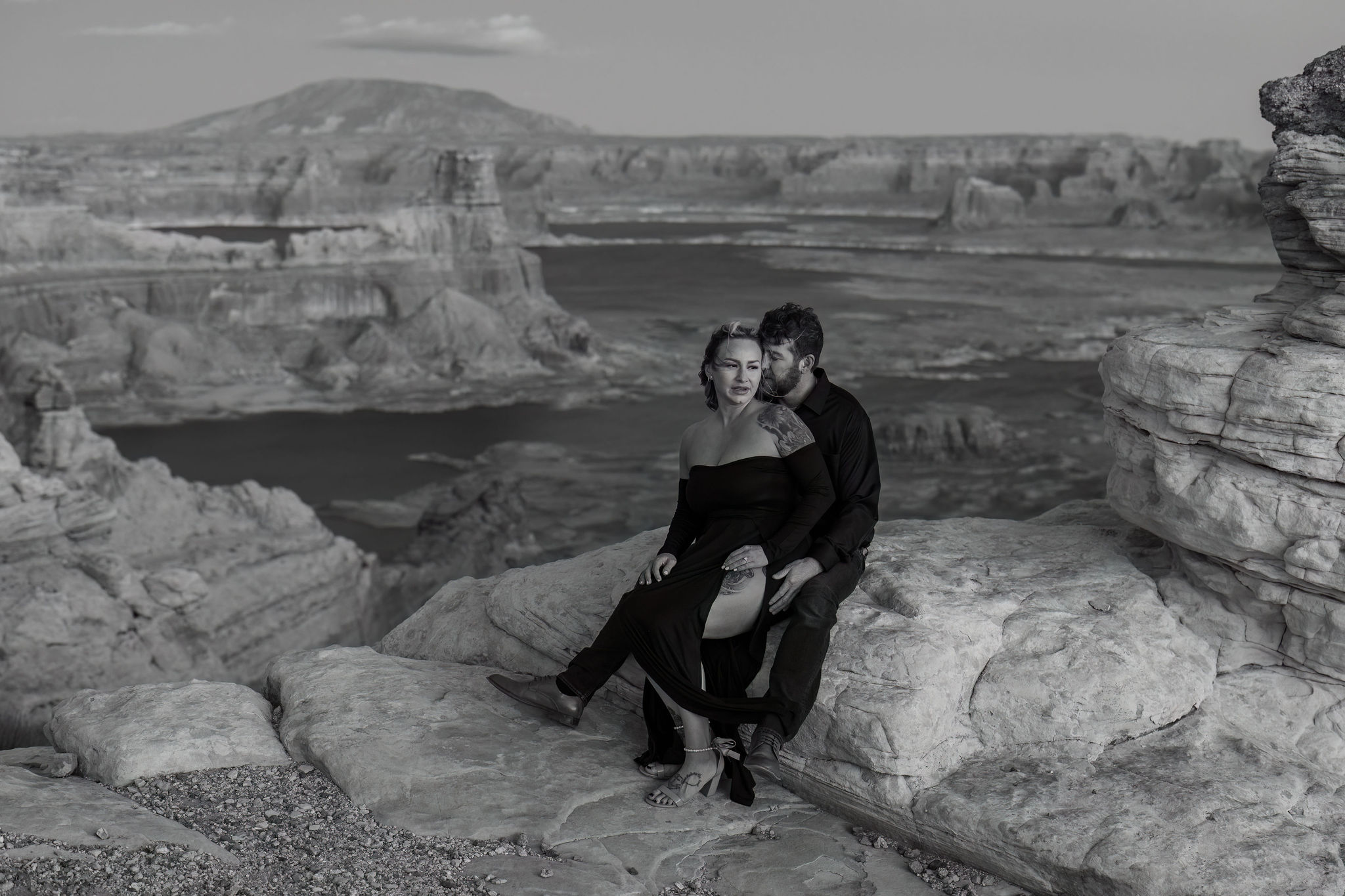 black and white of the couple sitting on rock with the Lake behind them 