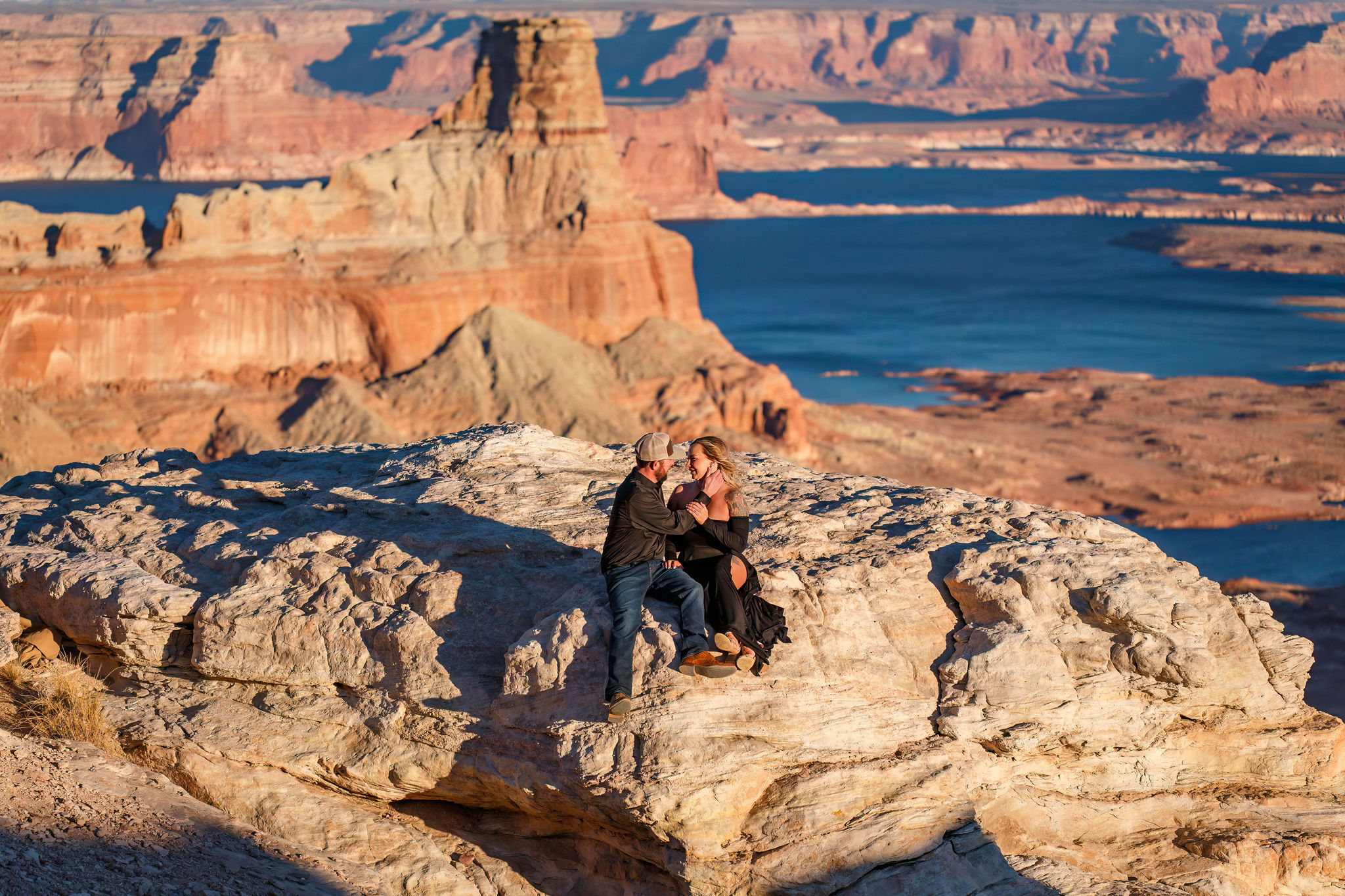 newly engaged couple sitting on the rocks with the incredible view of Lake Powell behind them 