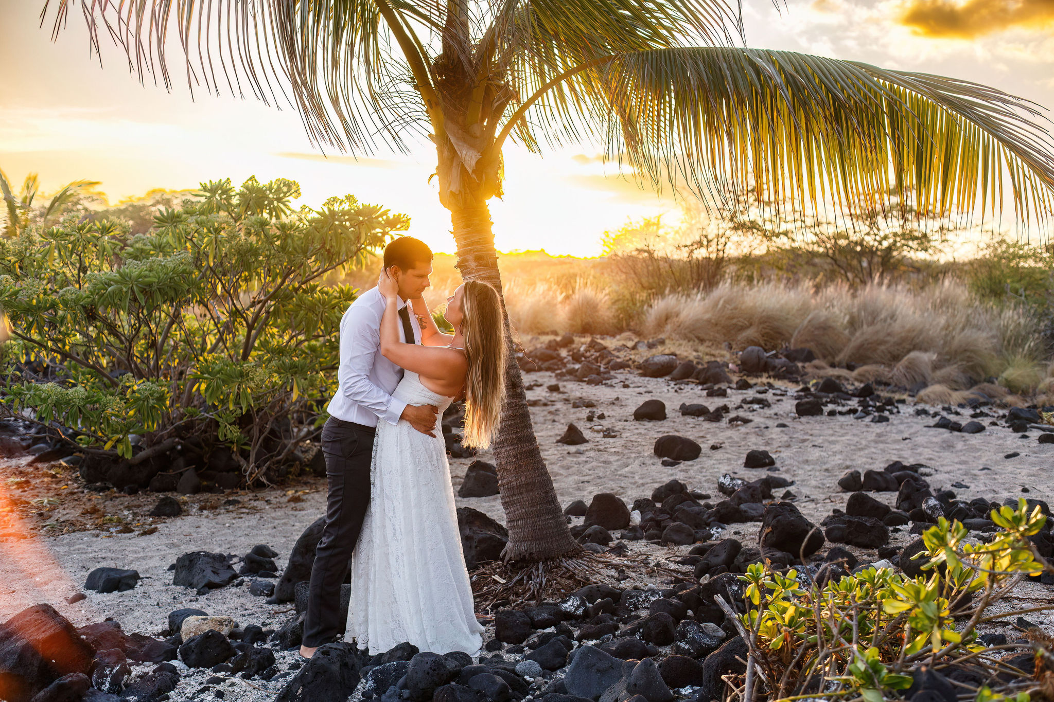 a couple standing on sand and black volcanic rocks on the beach in Hawaii 