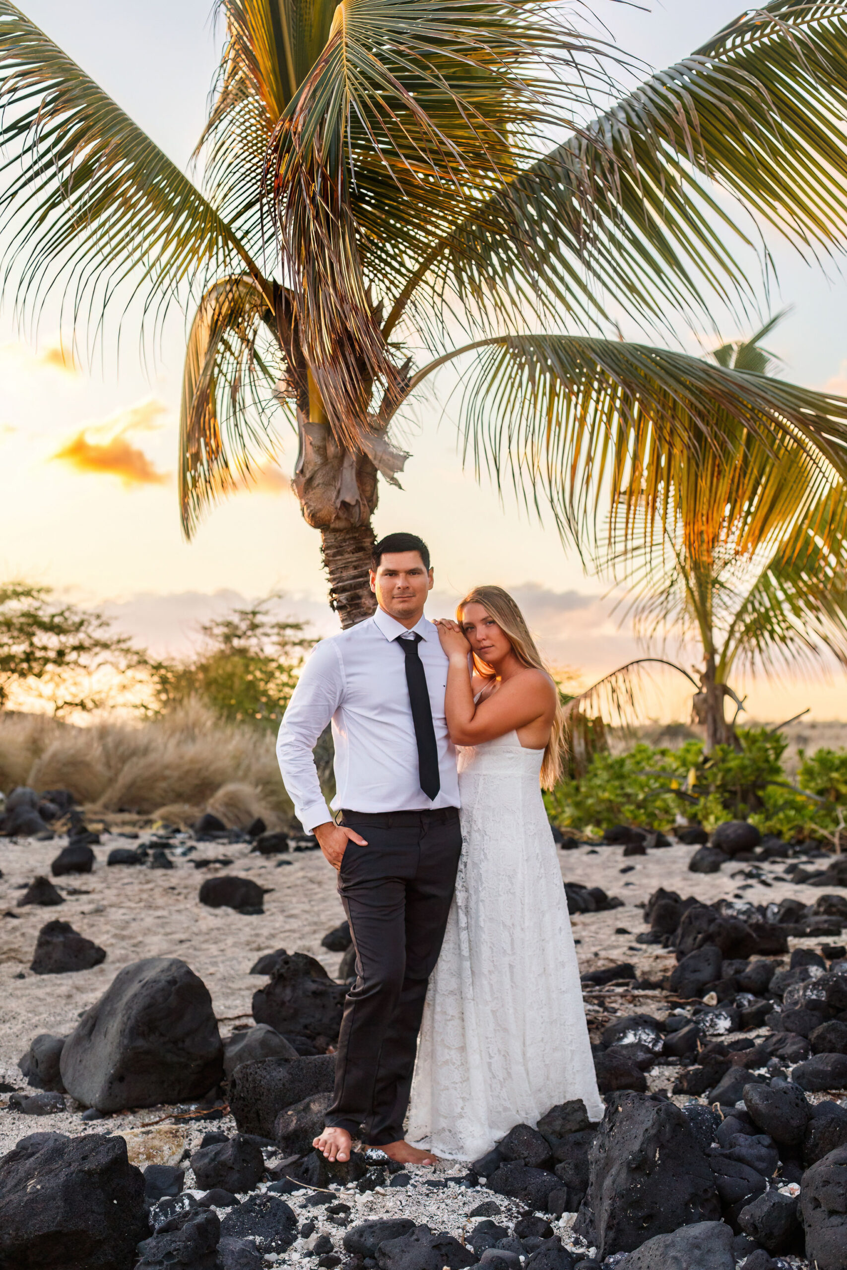 newly weds posing in front of a palm tree on the beach 