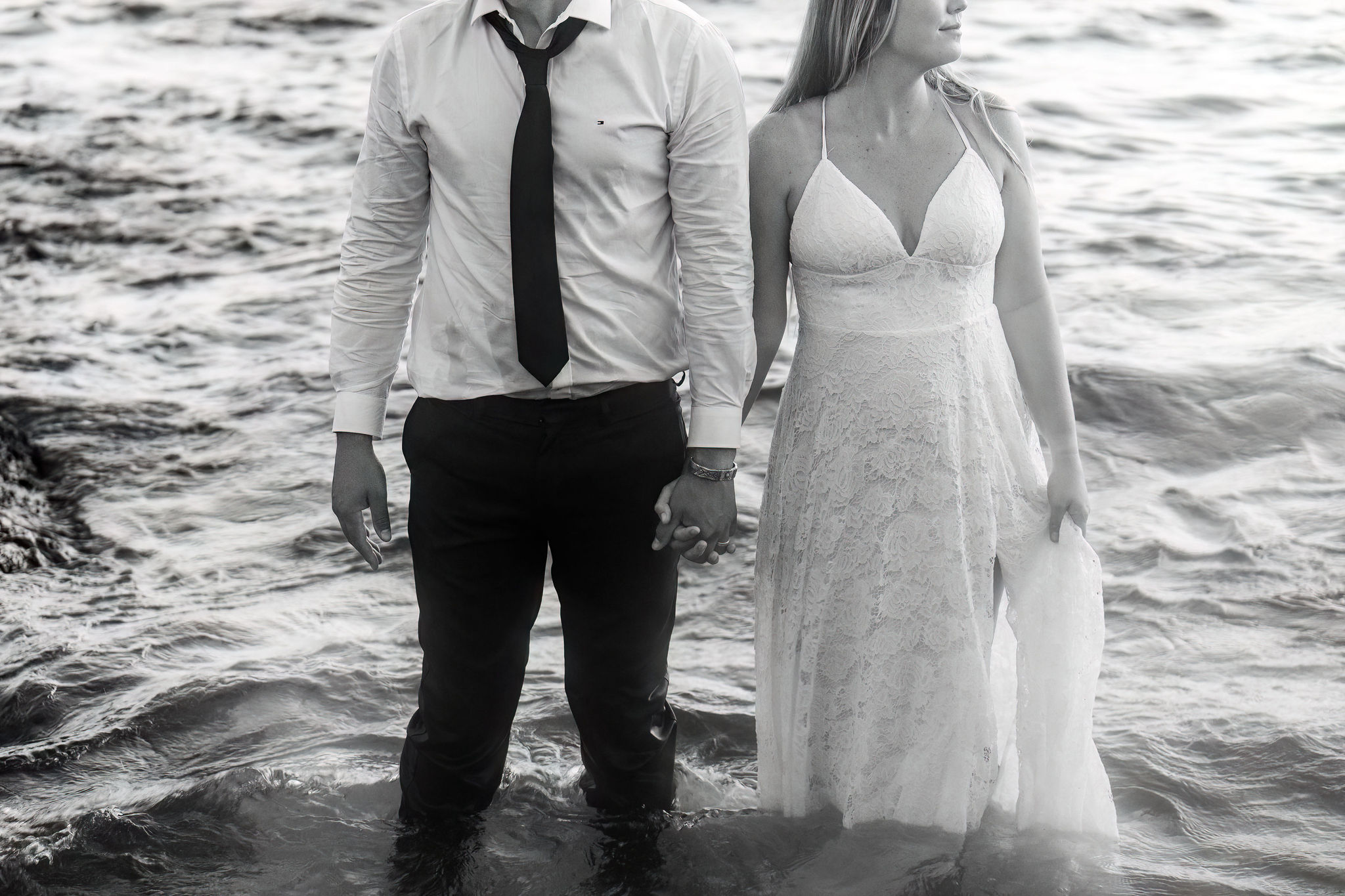 a couple holding hands while standing in the ocean in their wedding attire 