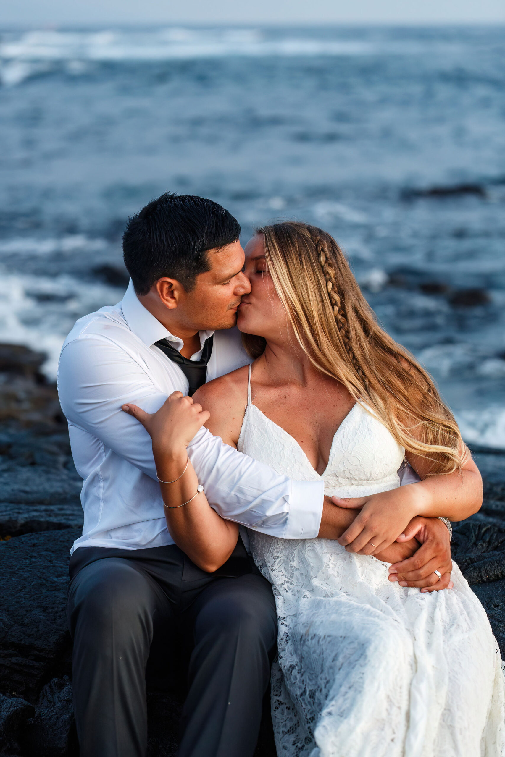 newly weds kissing as they sit on the rocky beach in Hawaii 