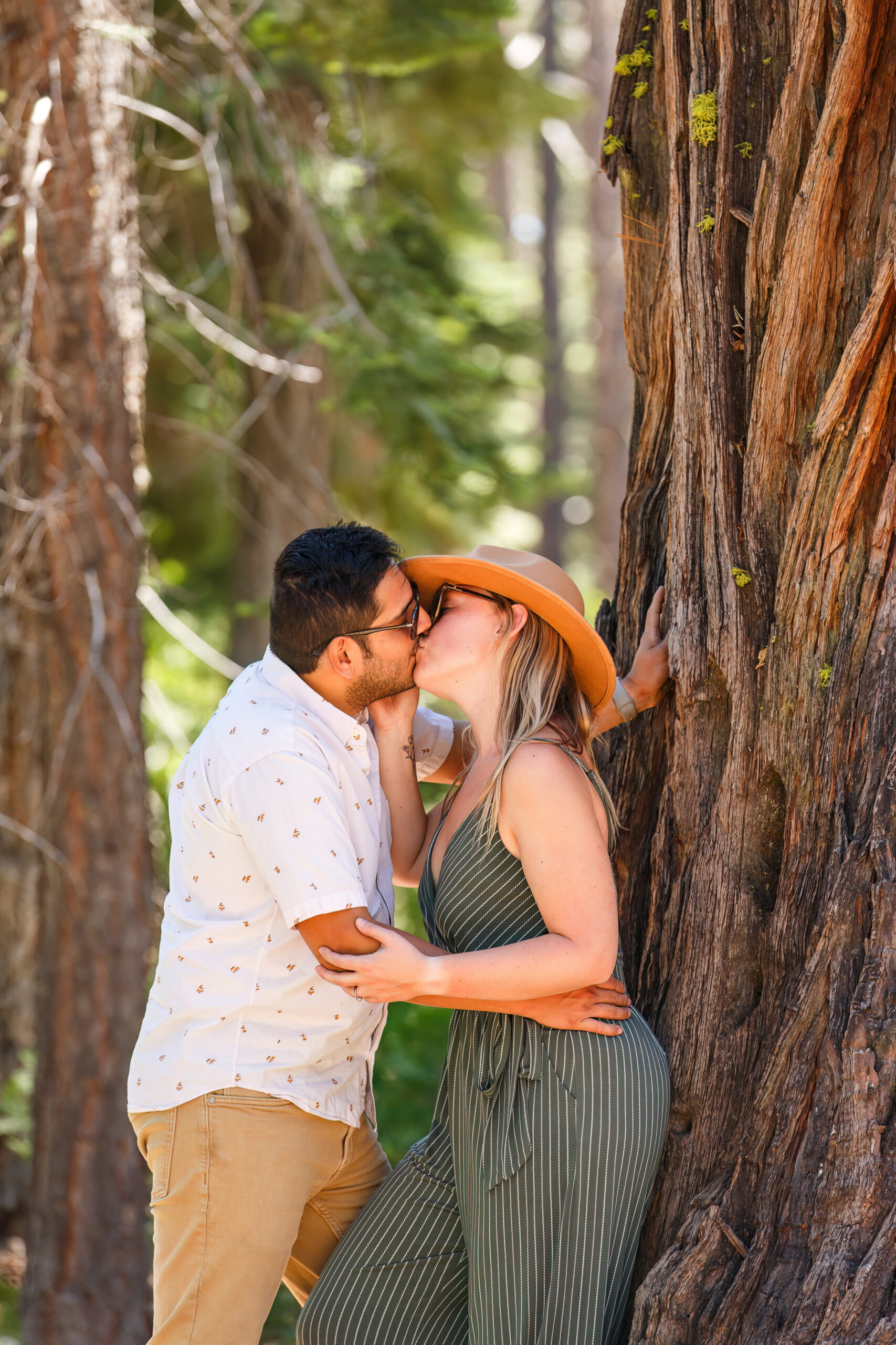 newly engaged couple kissing against a tree