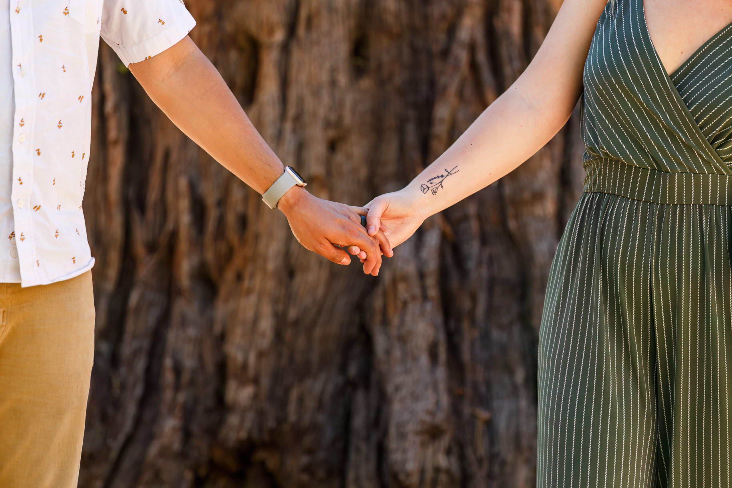 the couple holding hands as they walk through the trees