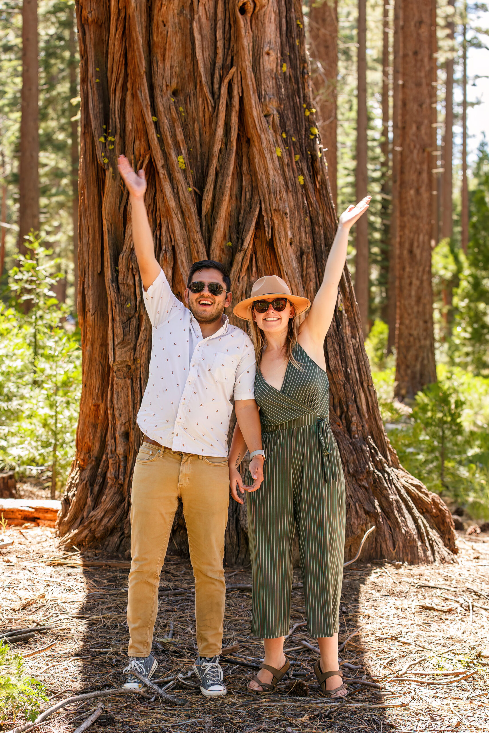 a couple standing in front of a tree with their hands up in the air