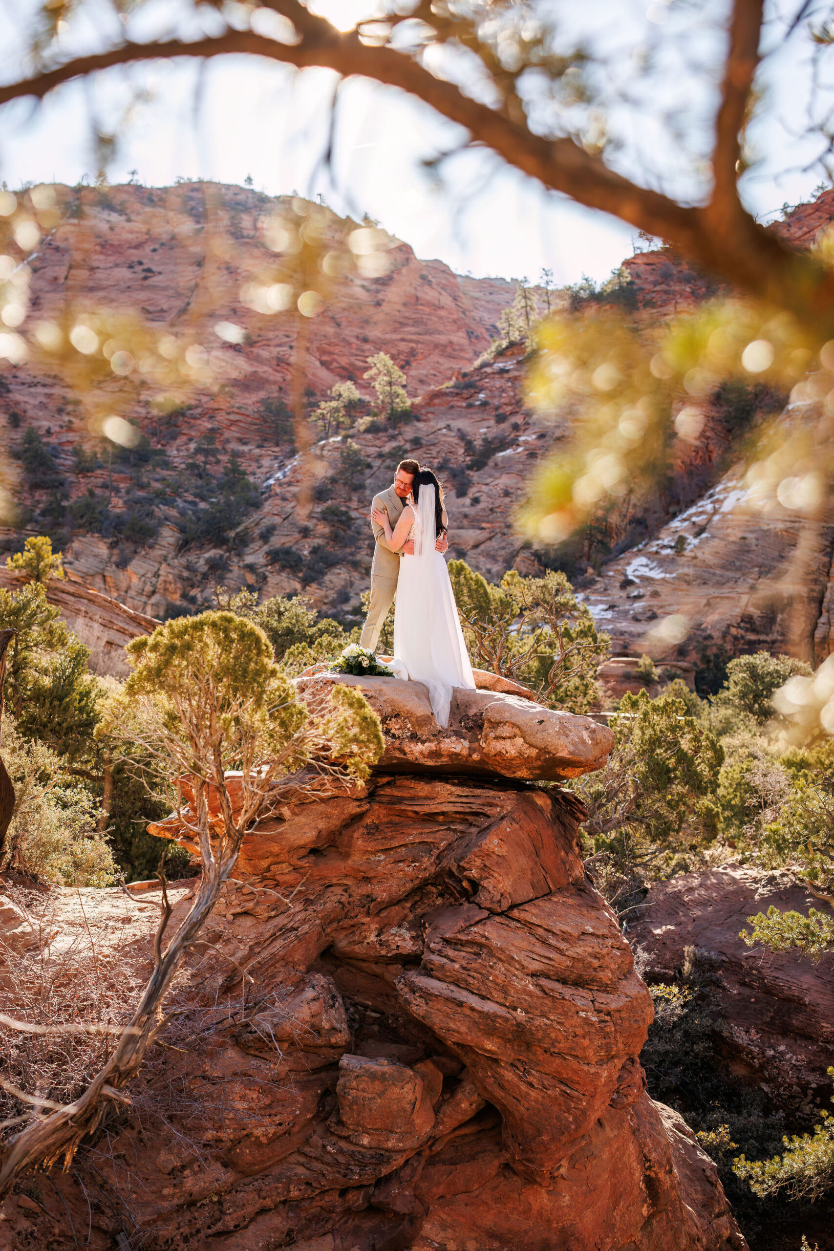 newly weds hugging while standing on a rock tower in Zion
