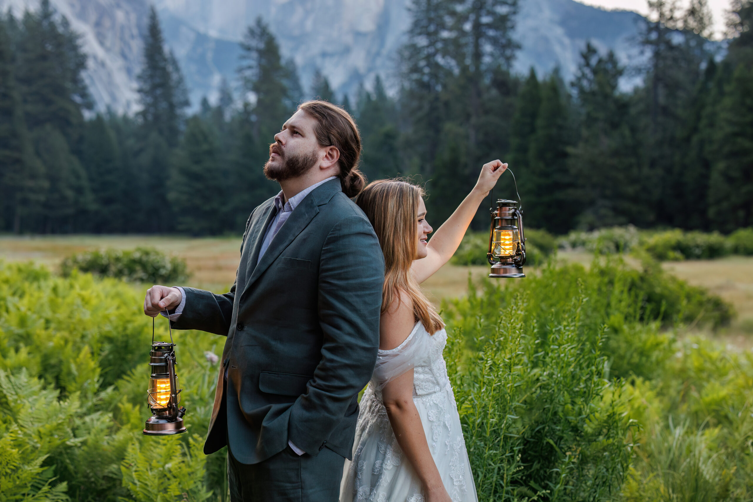 the couple back to back, holding lanterns, in a beautiful valley