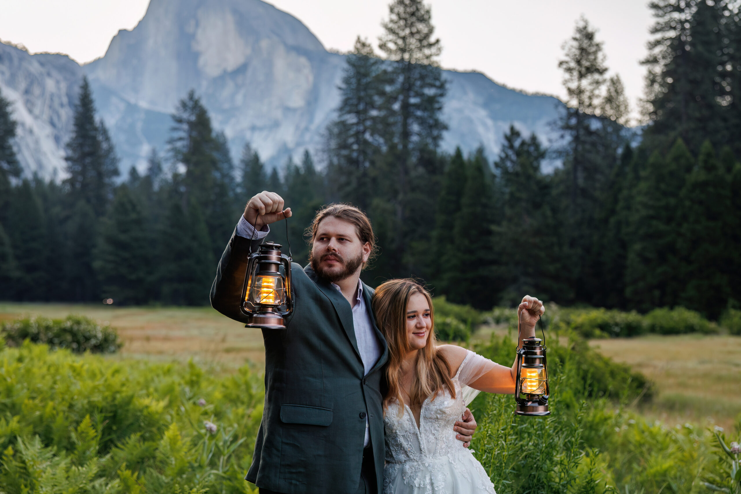 a couple in their wedding attire holding up lanterns as the sun comes up in Yosemite