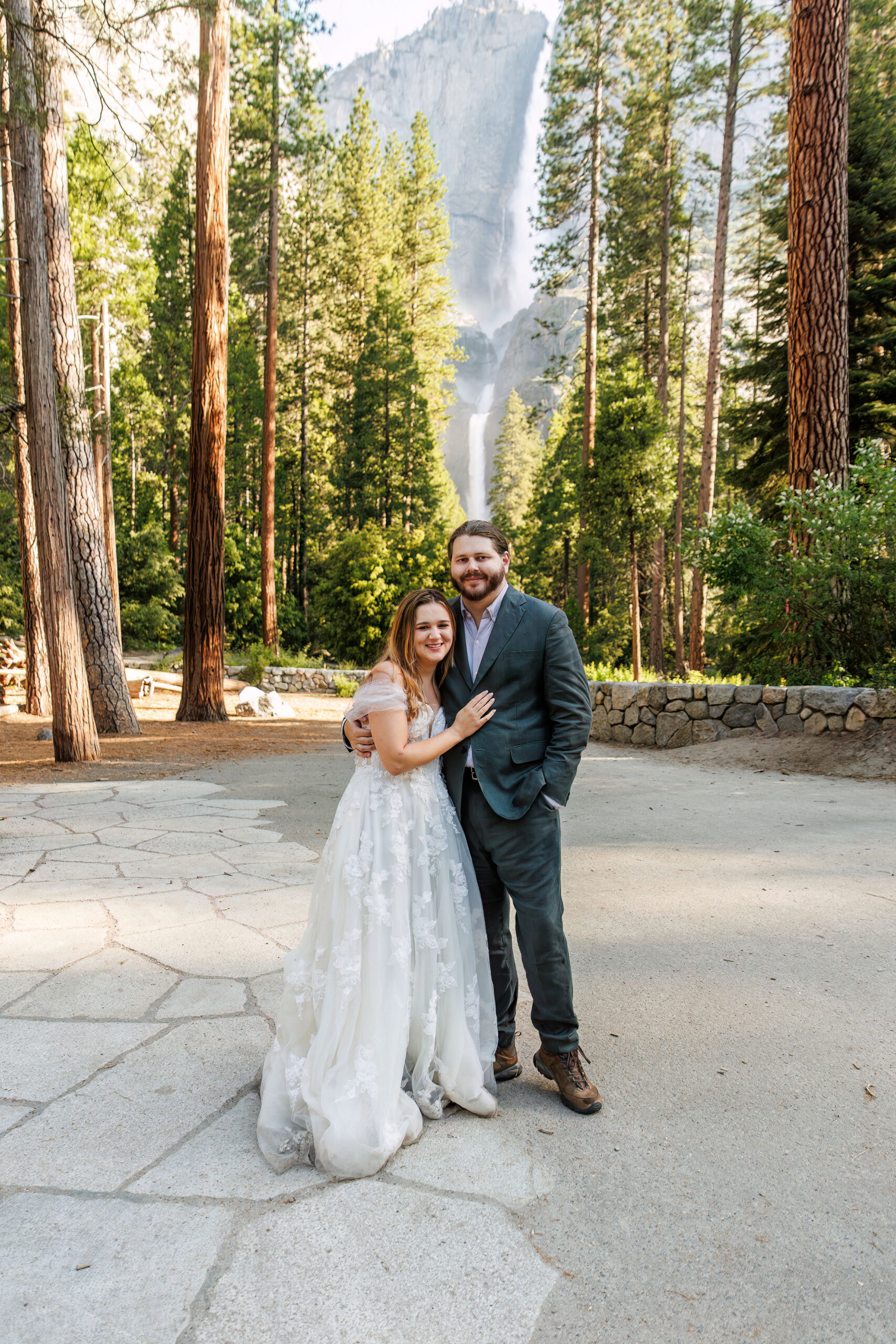 the newly weds smiling at the camera with a waterfall behind them