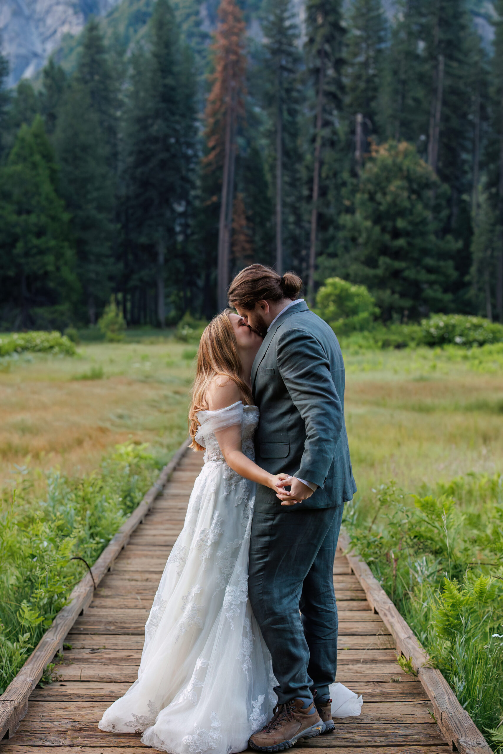 newly weds holding each other as they kiss on a wooden path for Yosemite wedding photos