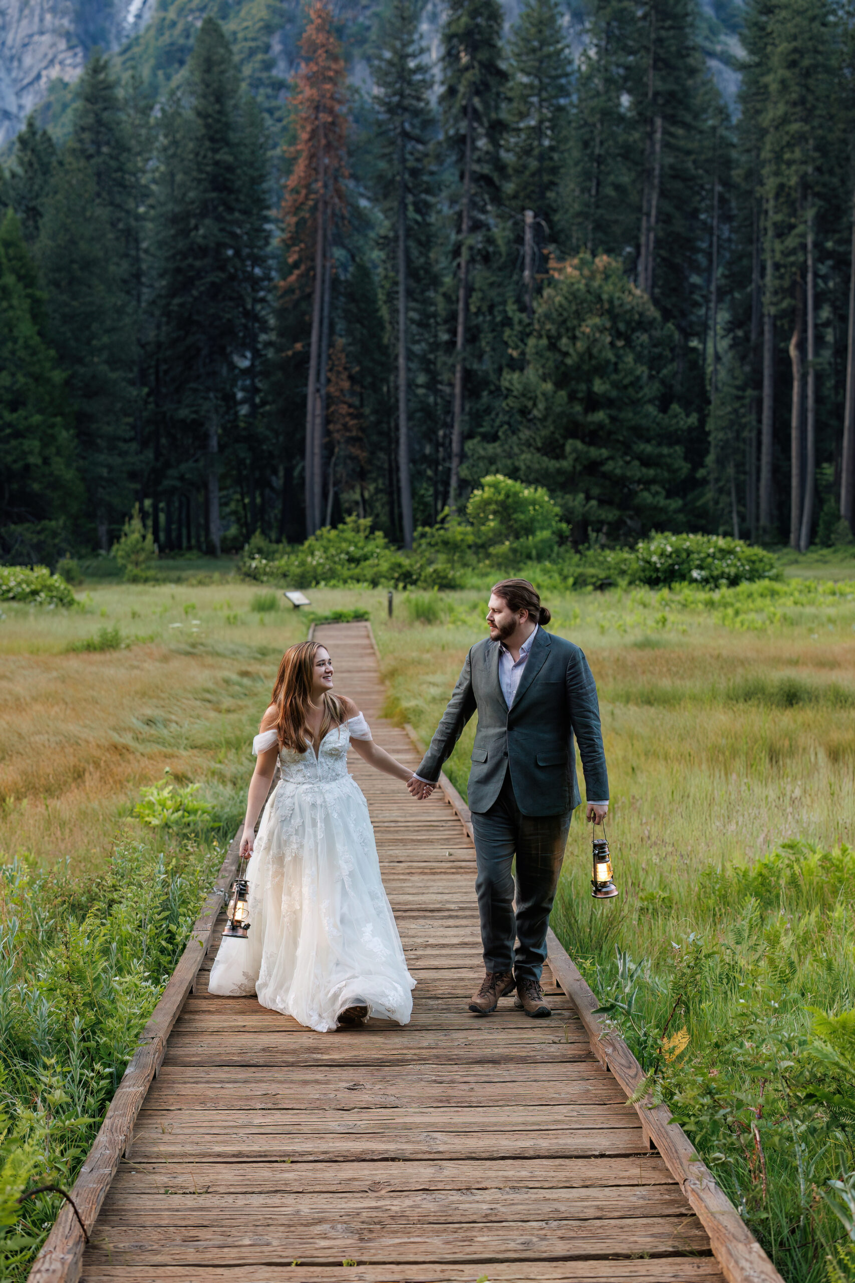 newly weds walking along a wooden path as they hold lanterns during their Yosemite wedding photos