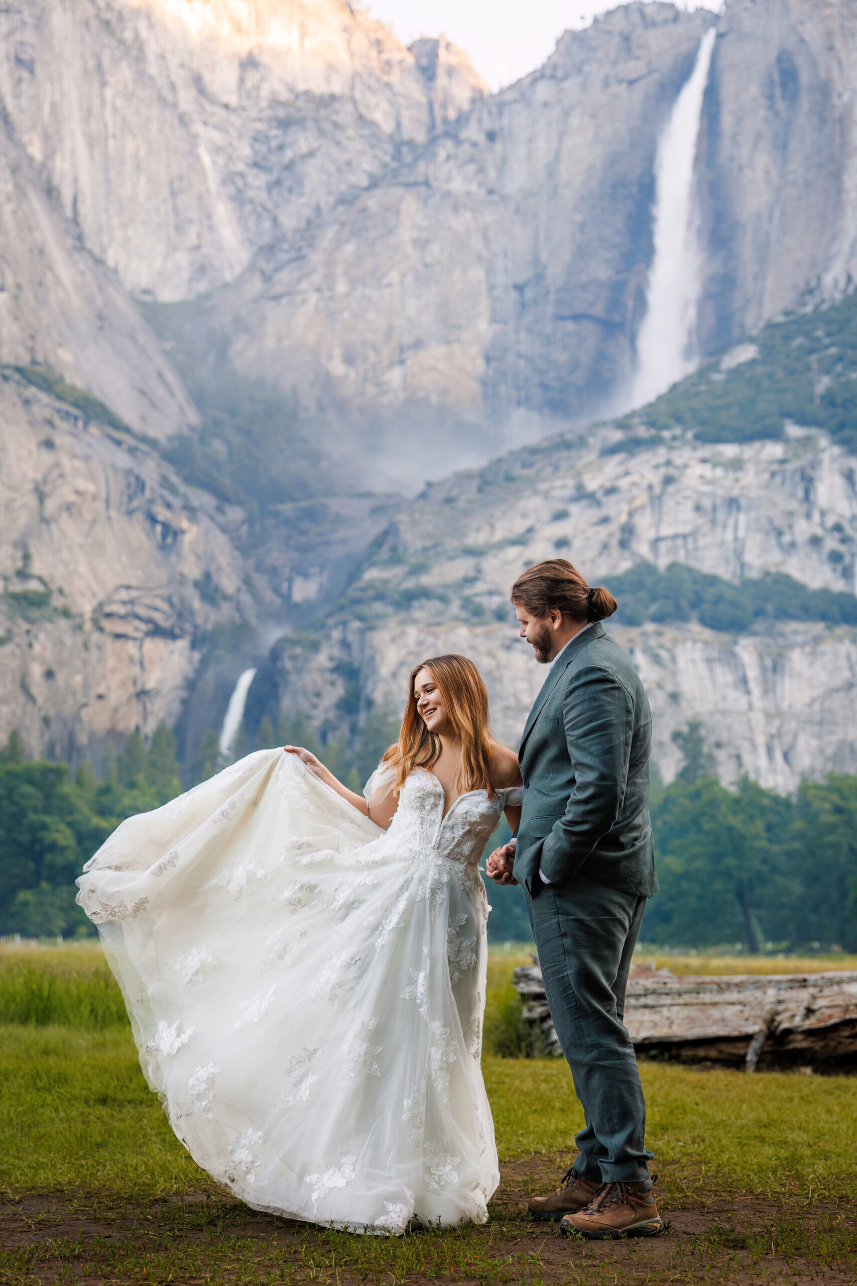 a bride holding out her dress as the groom admires her with a mountain and waterfall in the background