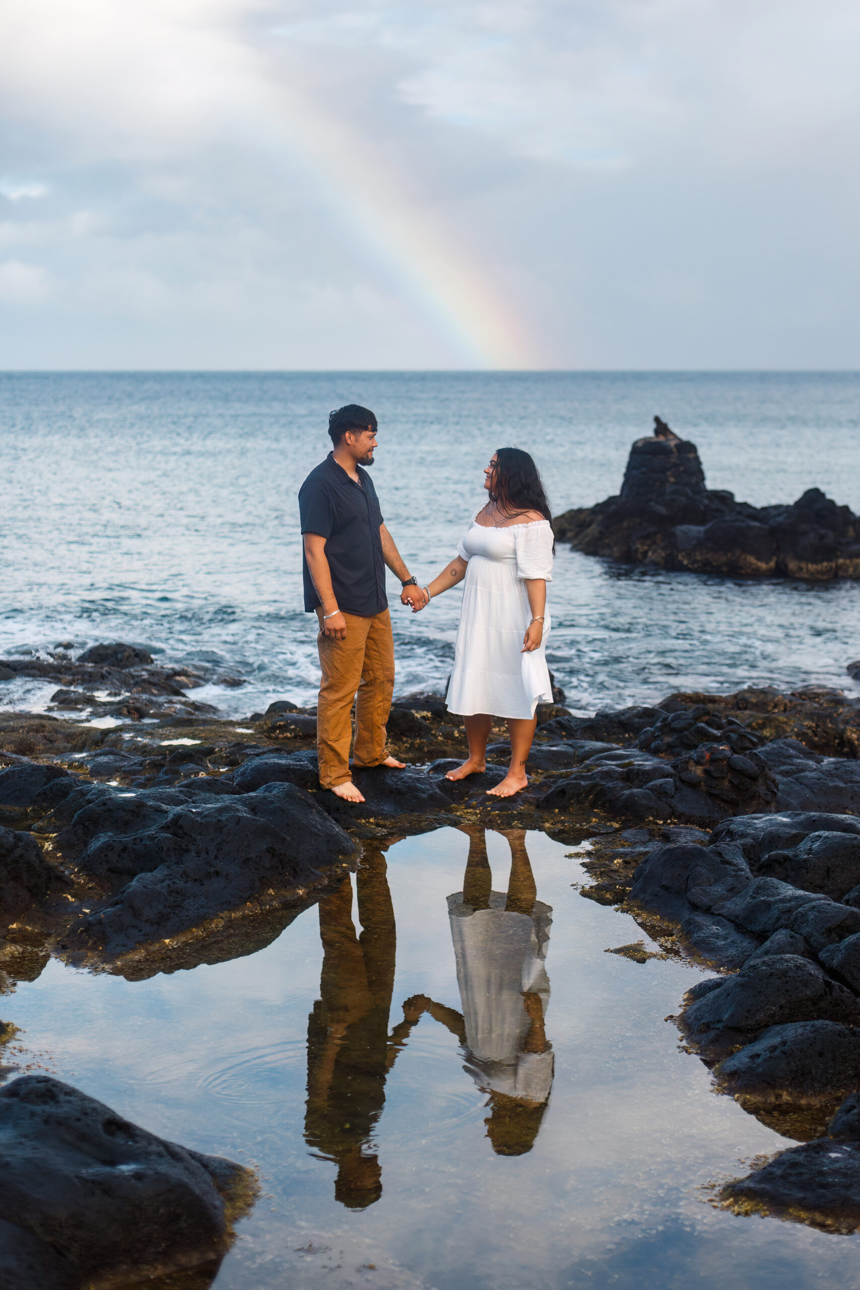 a couple standing holding hands with a rainbow behind them