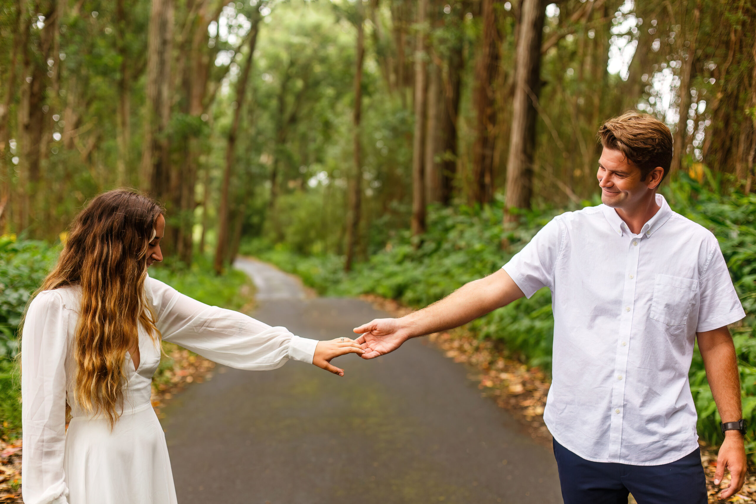 a couple smiling and holding hands as they walk on a path