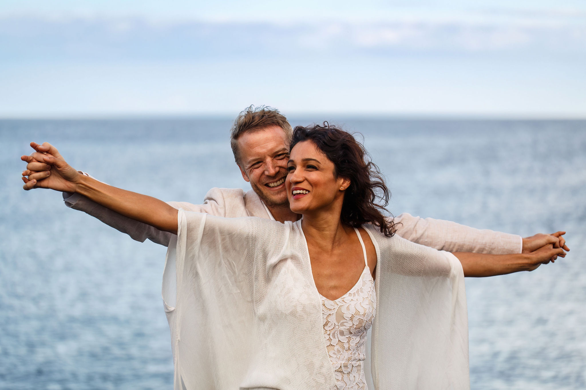 a man holding a woman's arms out with his on the beach