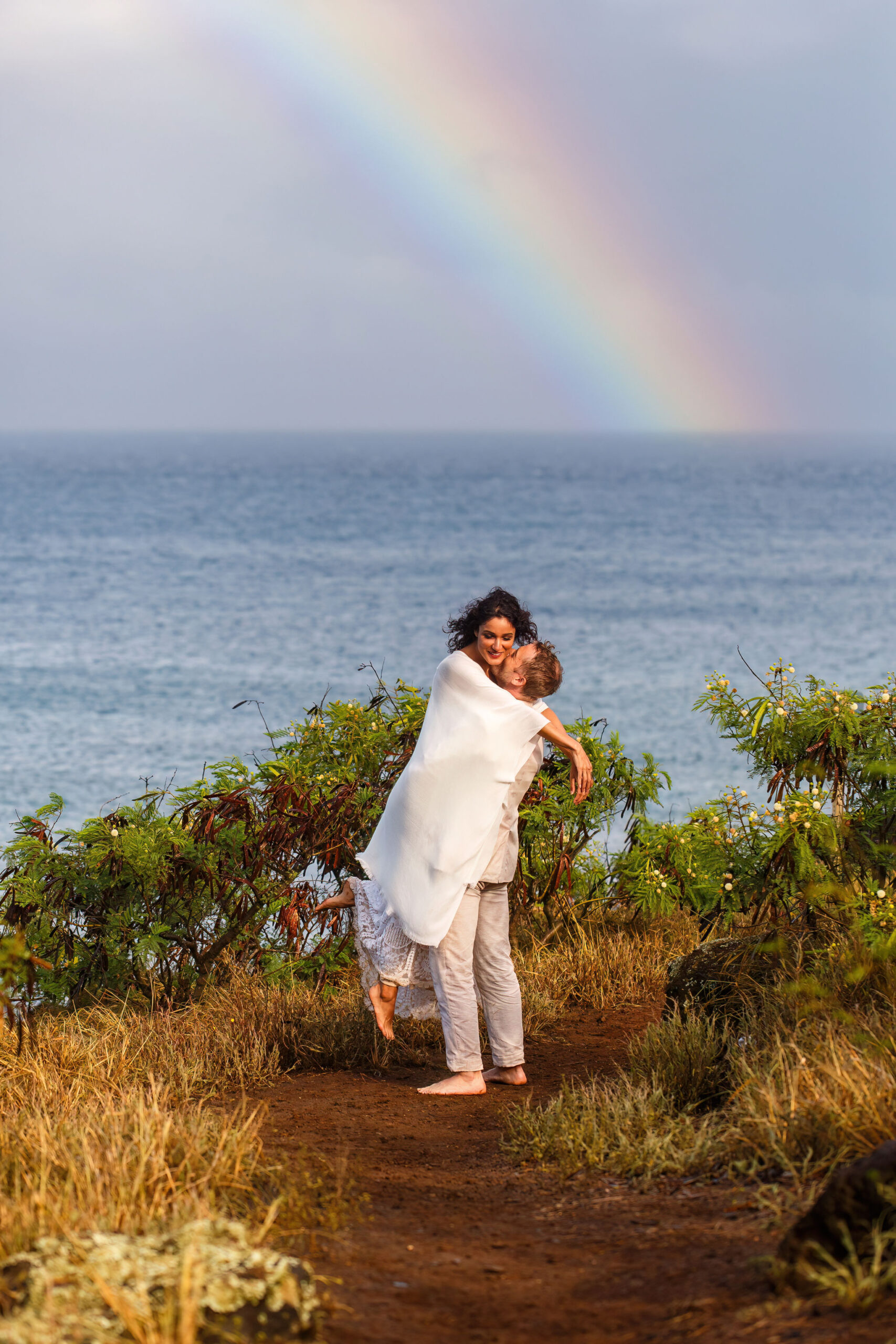a man picking up a woman and smiling with a rainbow behind them