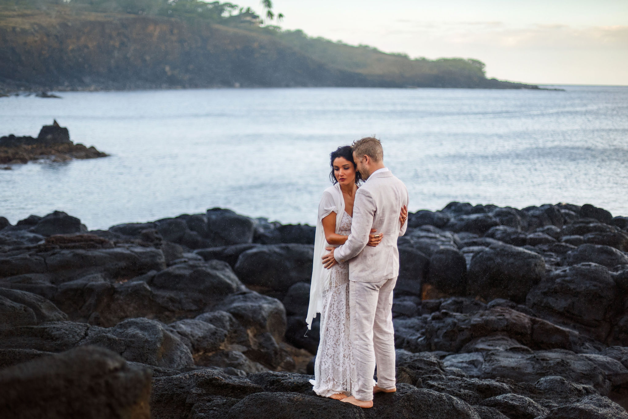 newly weds standing on black rocks by the ocean for their Hawaiian elopement