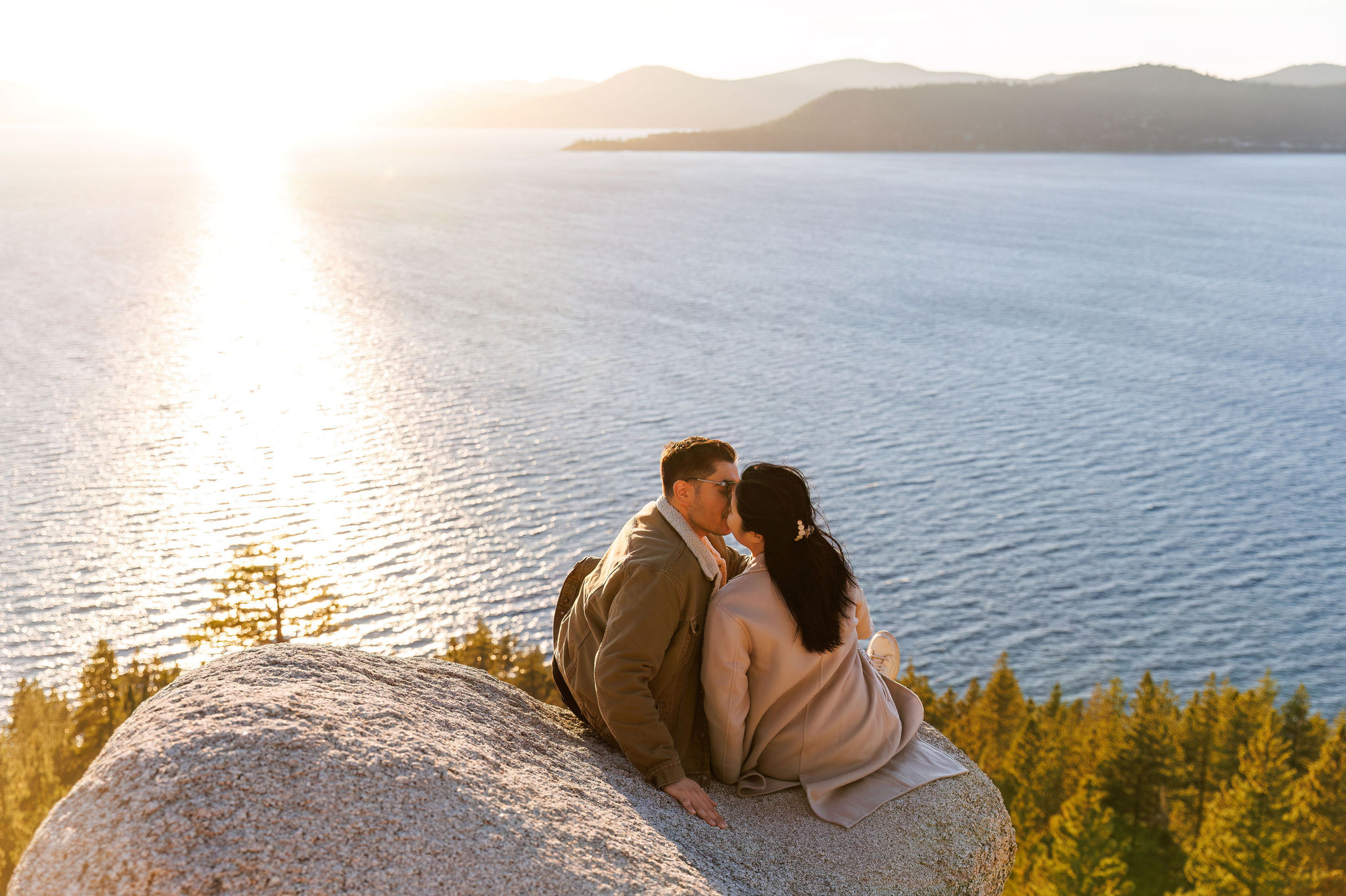 a couple sitting on a boulder at sunset