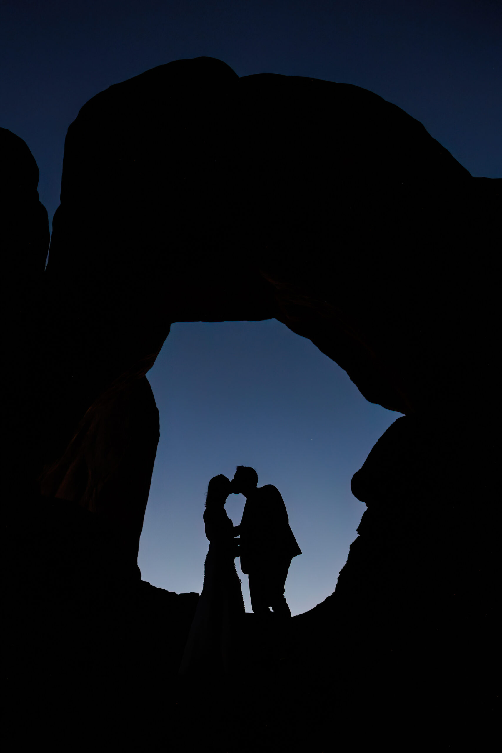 a couple underneath a desert arch, at the end of their elopement timeline