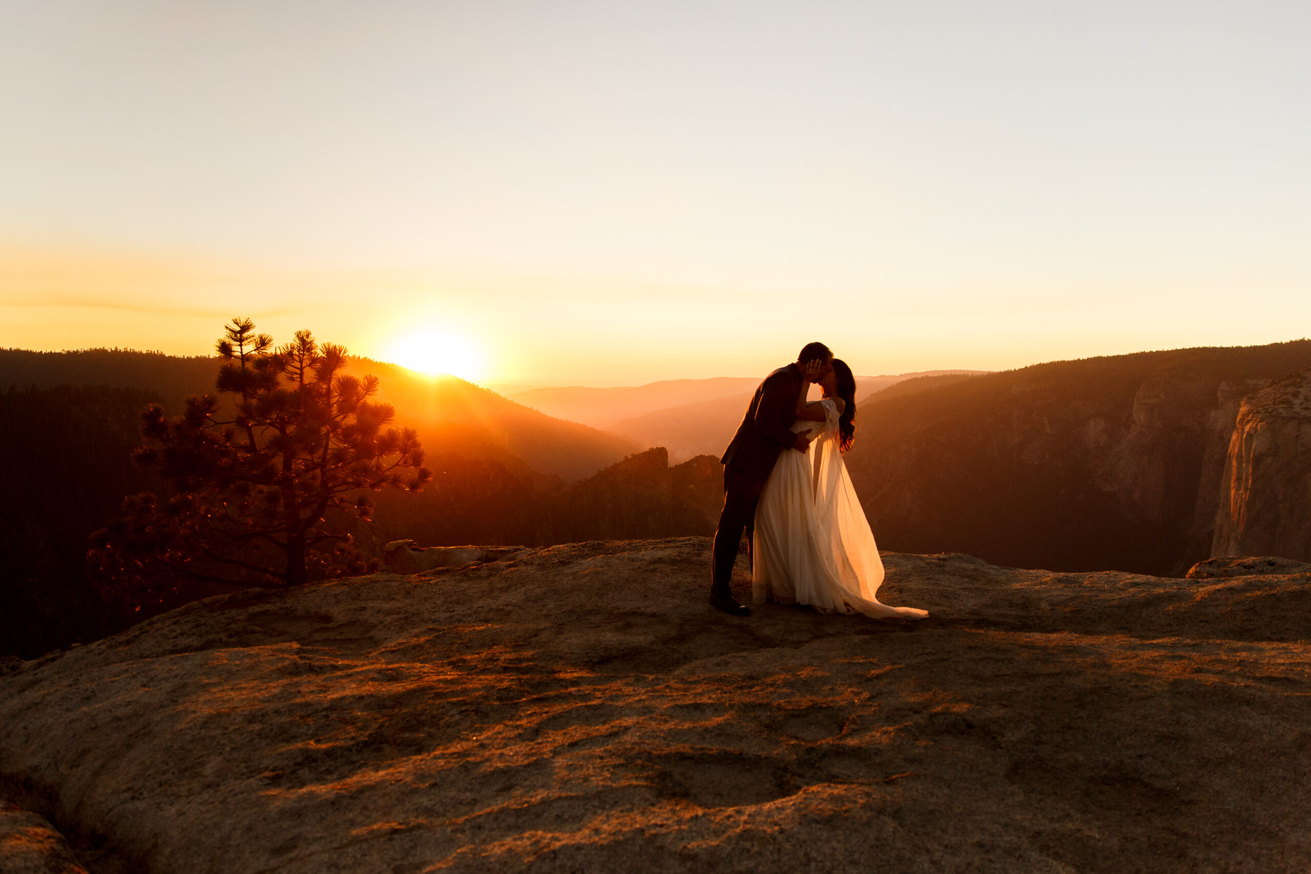 a couple kissing on top of a mountain at sunset