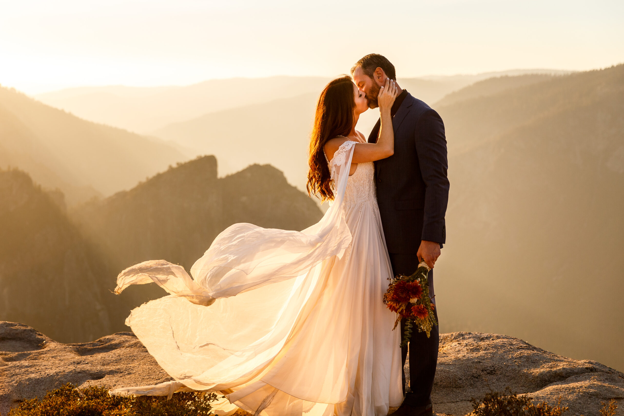 newly weds kissing on top of a mountain