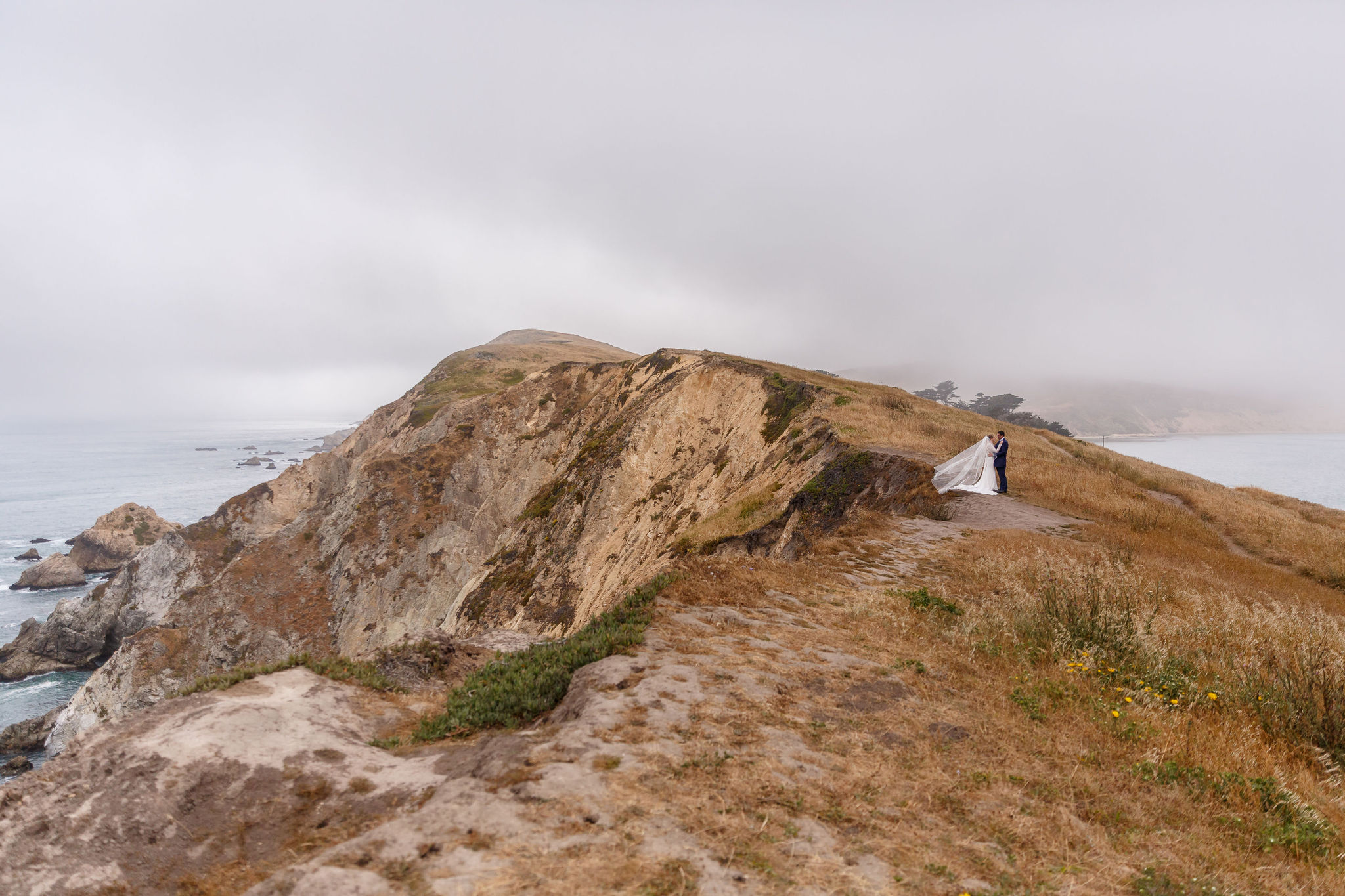 a couple on a cliff with fog rolling in for their Point Reyes elopement