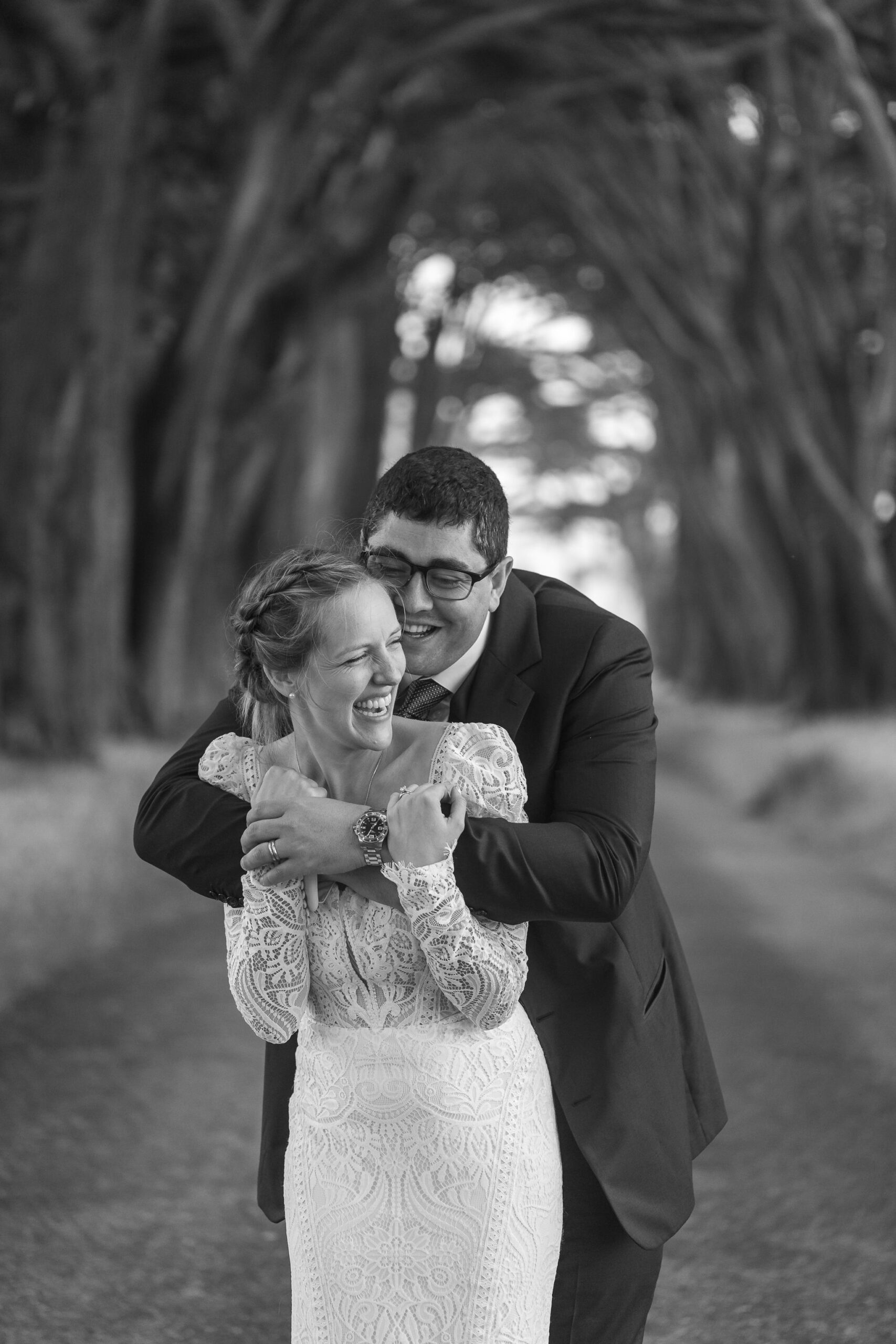 the groom holding the bride from behind as they smile