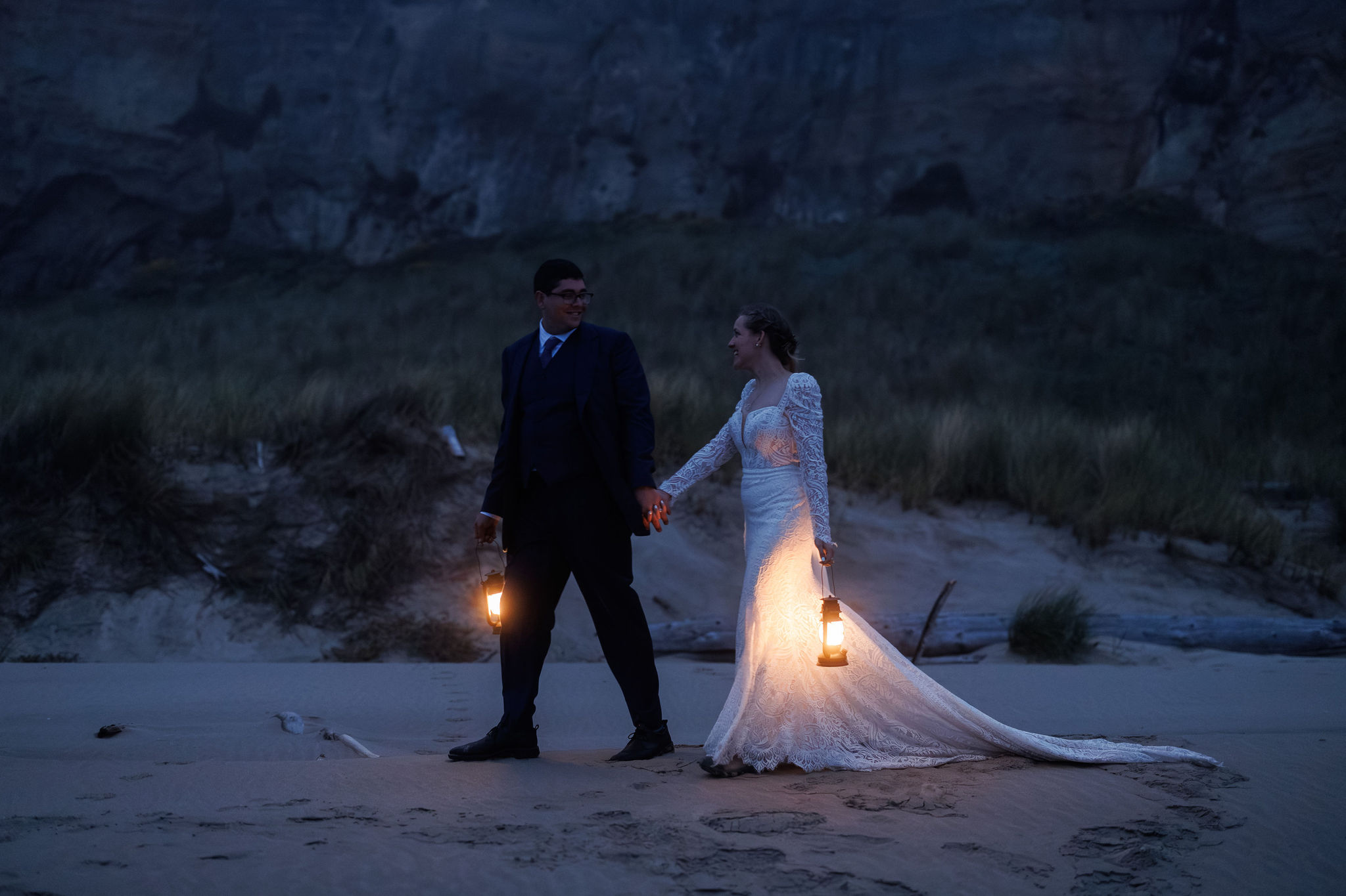 a couple walking on the beach at night holding lanterns