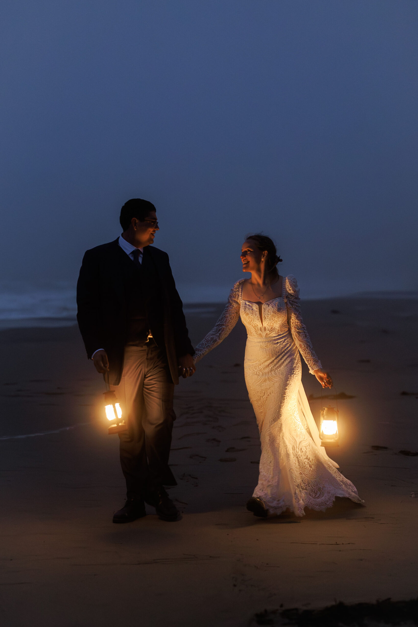 newly weds walking on the beach with their lanterns illuminating their path